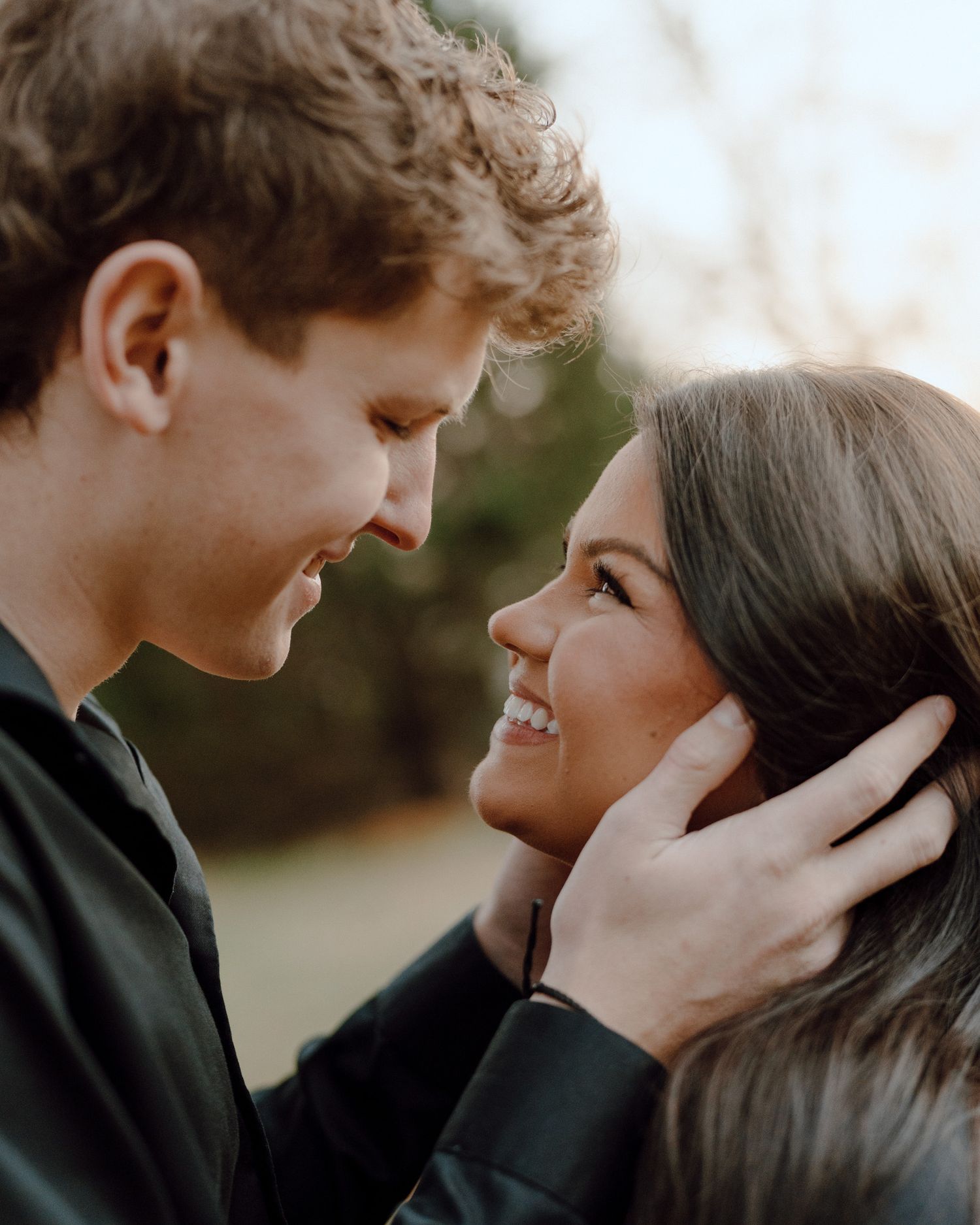 A tender romantic moment between a couple in dark clothing sharing an intimate close-up against a blurred background.