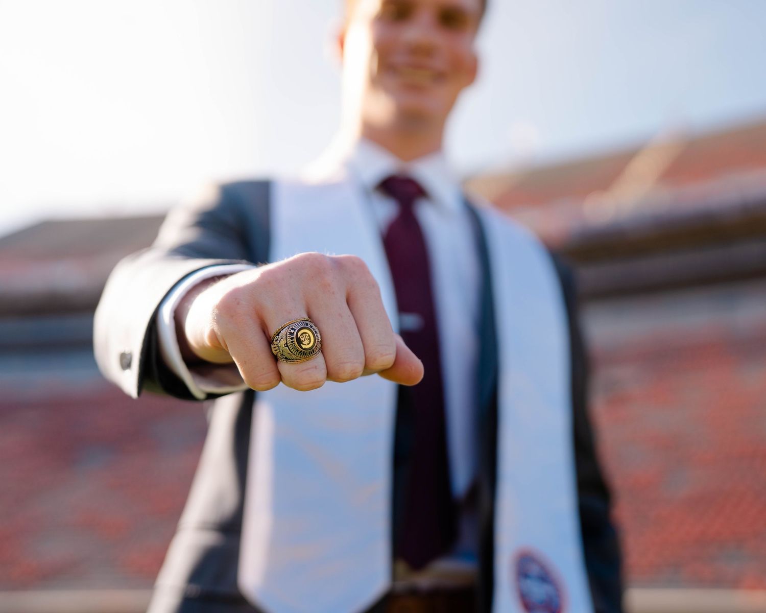 Close up of a hand wearing a championship ring against a stadium background.