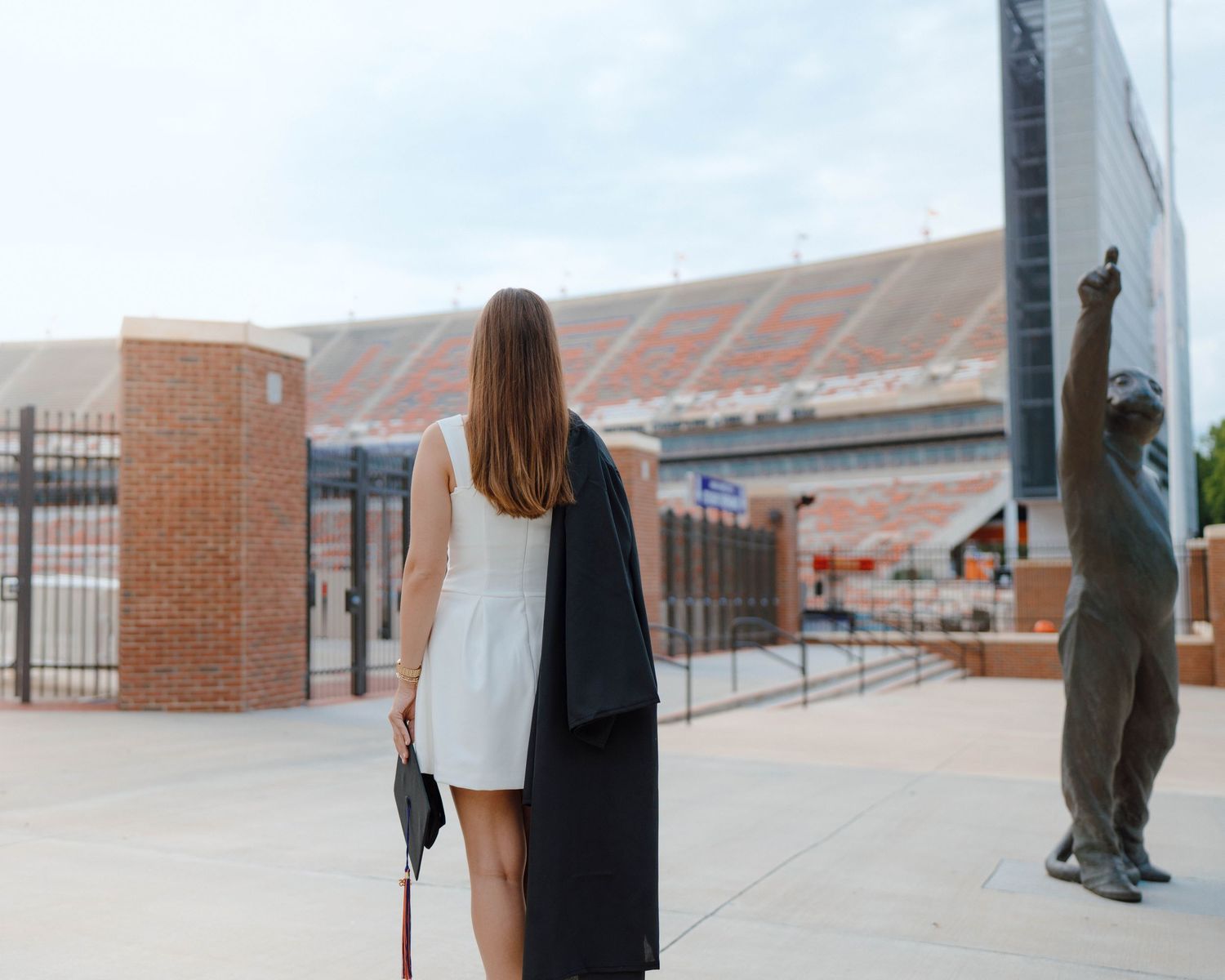 A person in a half-white half-black outfit stands near a sports stadium entrance with a statue visible in the background.