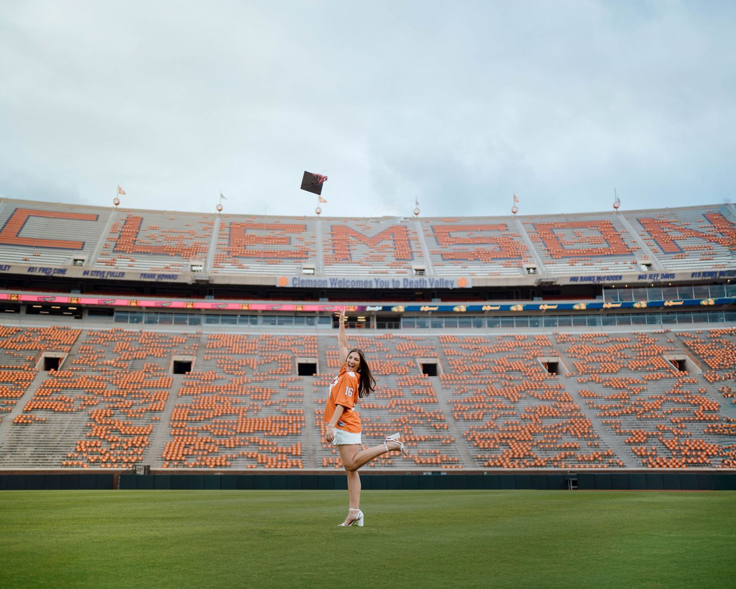 Orange stadium seats form the name 'CLEMSON' at Memorial Stadium while a cheerleader performs on the field.