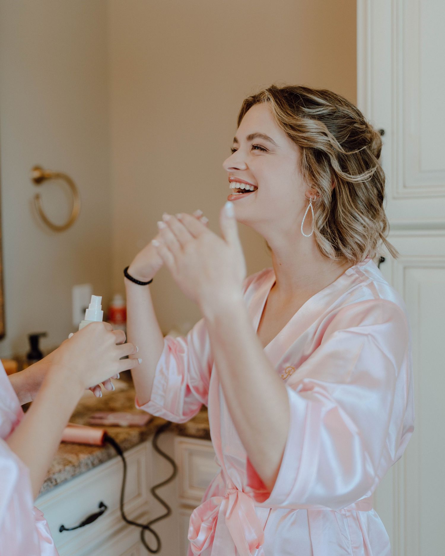Someone wearing a pink silk robe laughs joyfully while getting ready in a bathroom setting.