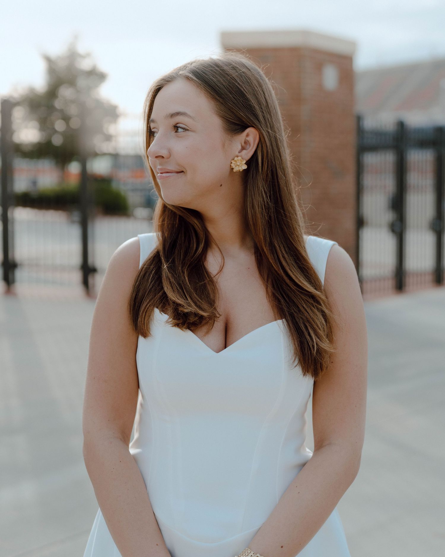 Young woman in white dress looking to the side with content expression on sunny day outdoors.
