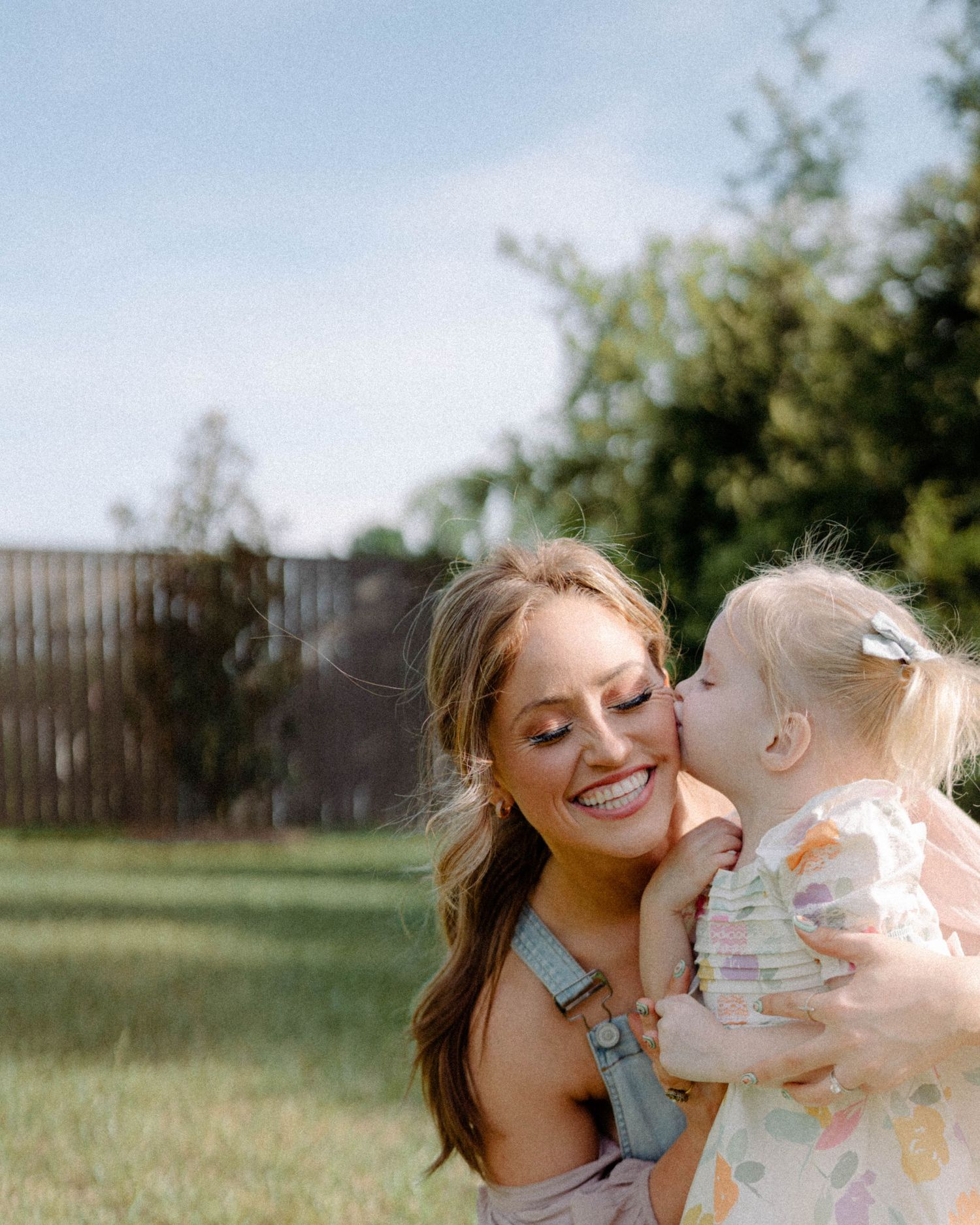 A tender moment of joy and laughter between parent and child as they embrace in a sunny backyard garden.