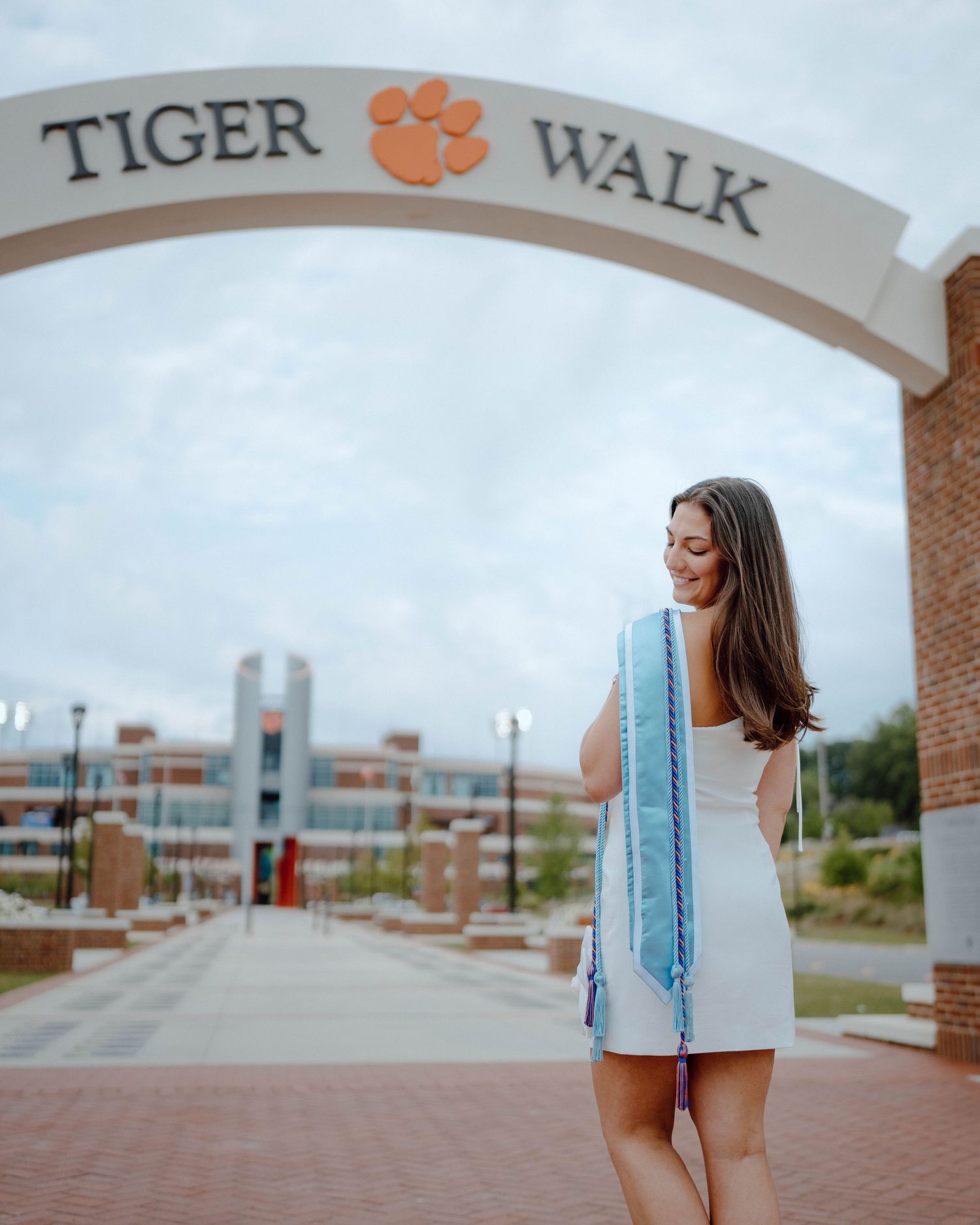 Student stands under Tiger Walk archway on a cloudy day at Clemson University campus.
