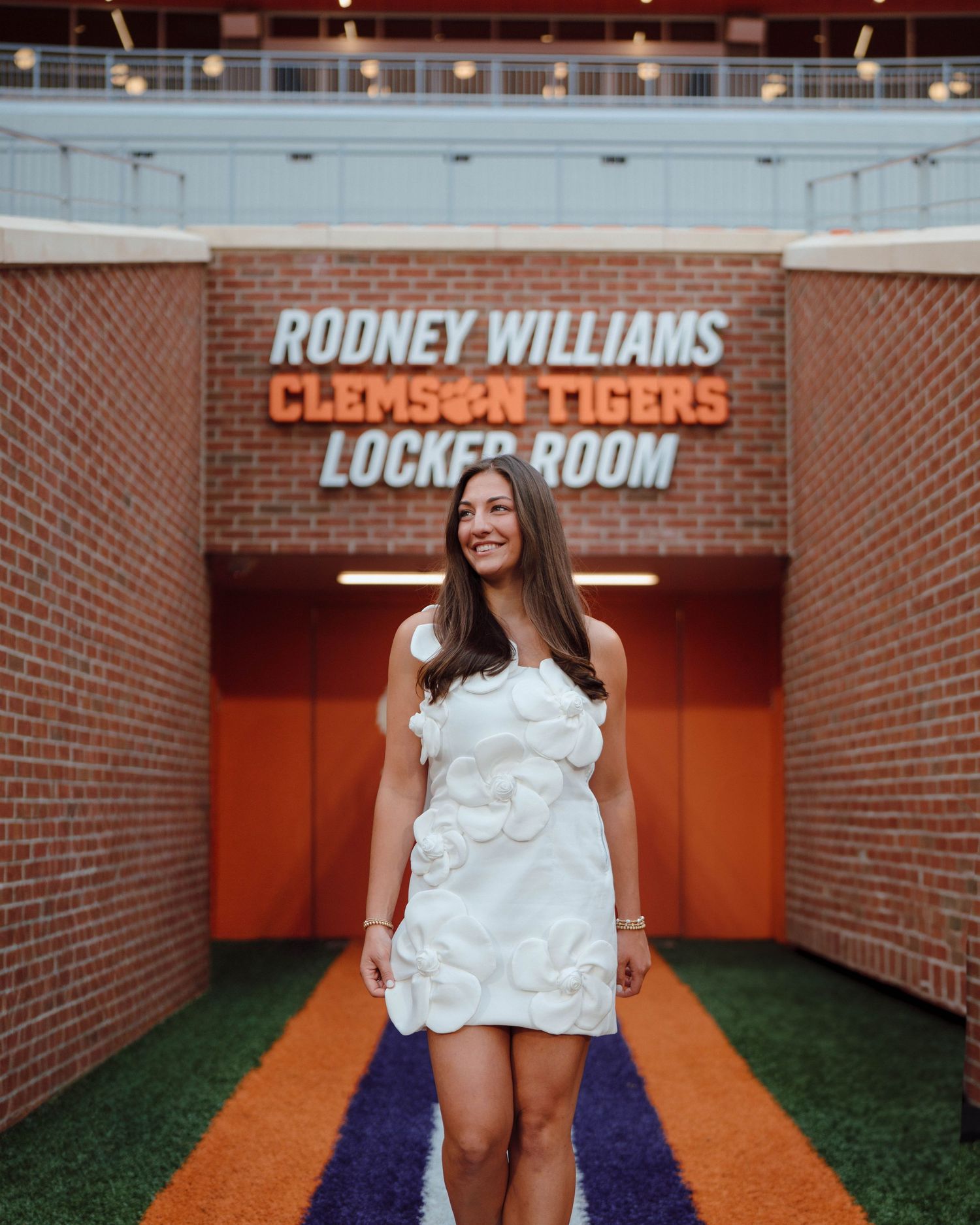 White dress at Clemson Tigers locker room entrance with orange and purple carpet leading to Rodney Williams sign.