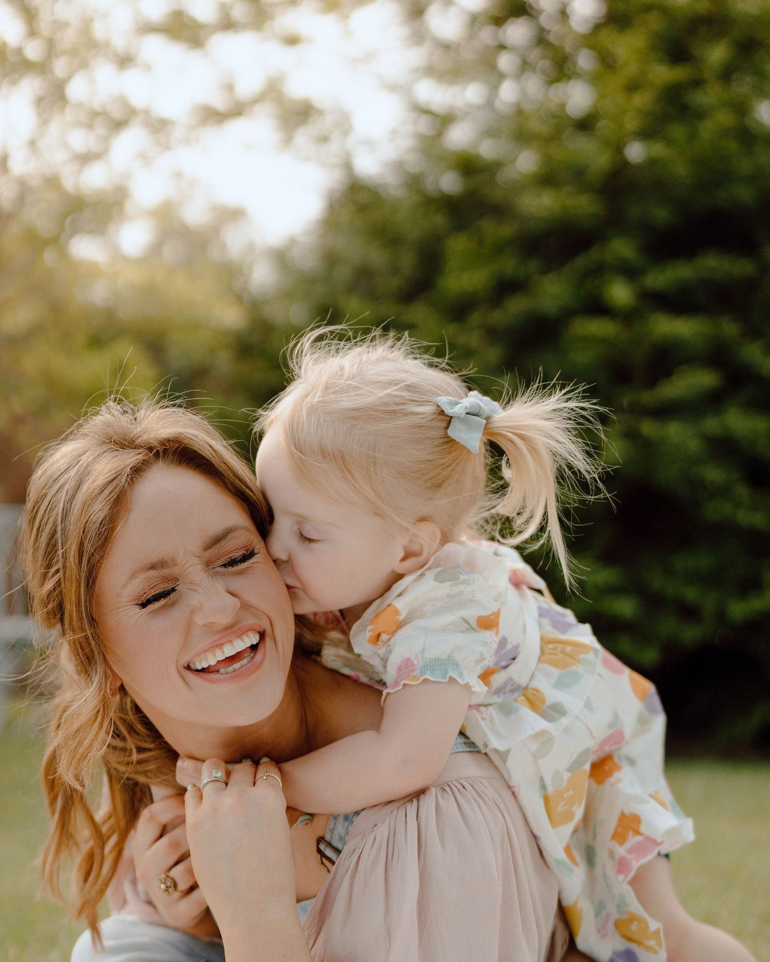 A joyful candid moment shared between a parent and child in an outdoor setting with greenery in the background.