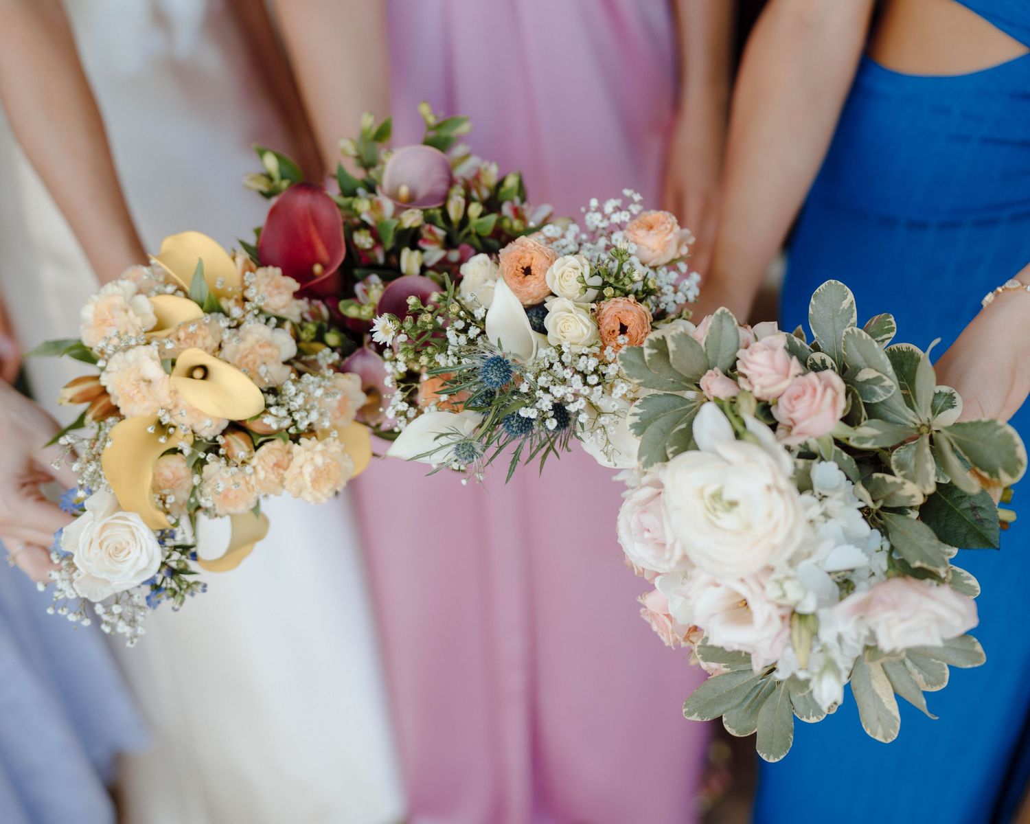 Bridesmaids in pastel dresses hold romantic bouquets featuring roses, eucalyptus and delicate wildflowers.