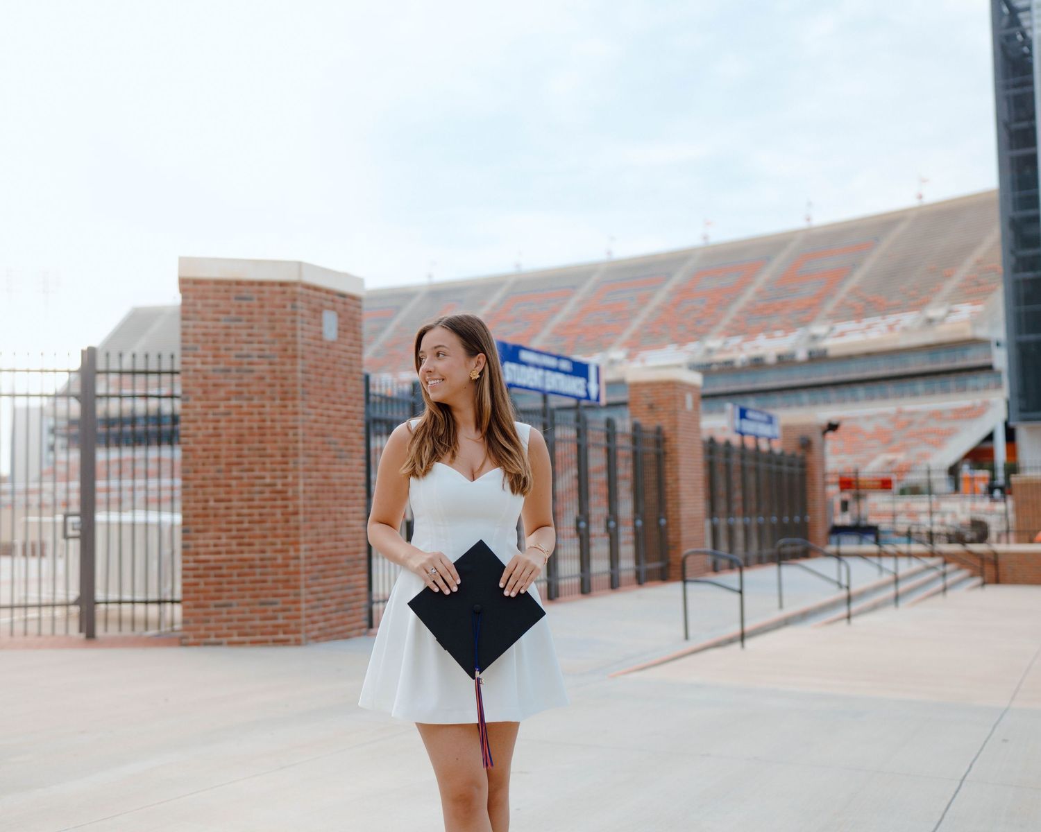 A person in a white dress stands outside a brick sports stadium on a sunny day.