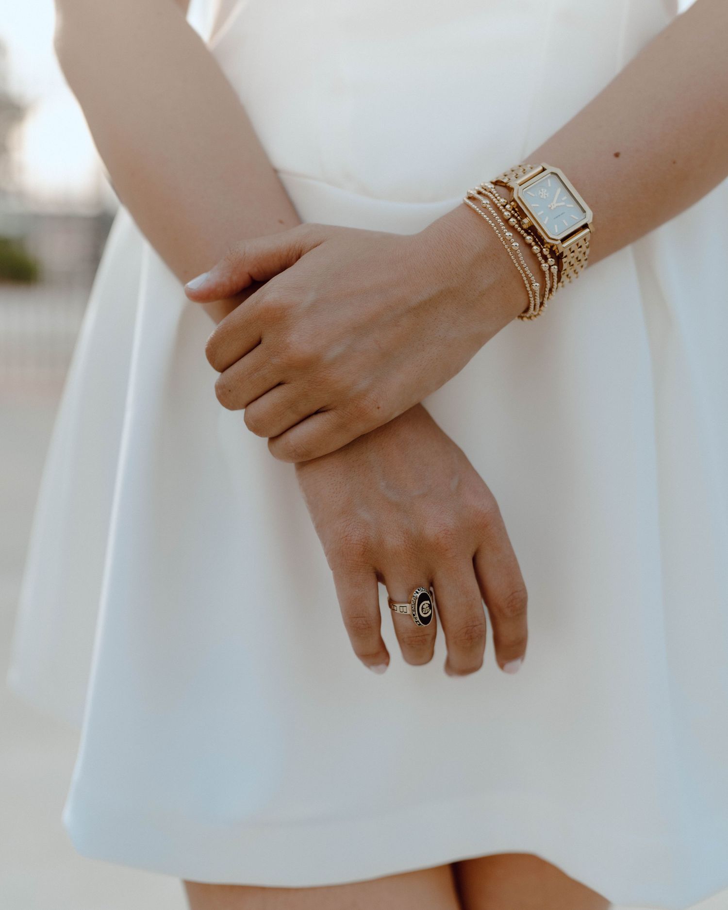 Close-up of hands wearing gold stacked bracelets and a statement ring against a white dress.