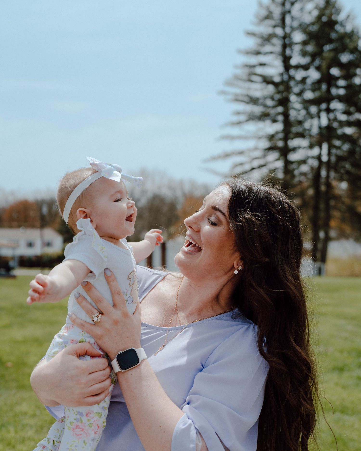 A joyful outdoor moment shared between parent and baby on a sunny day with evergreen trees in the background.