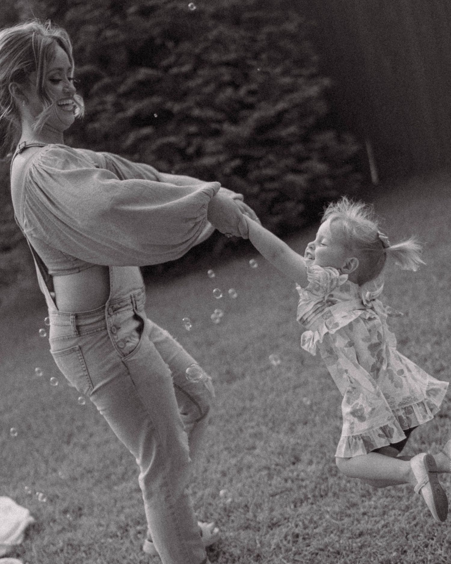 Two figures playing and dancing together with bubbles in a black and white outdoor scene.
