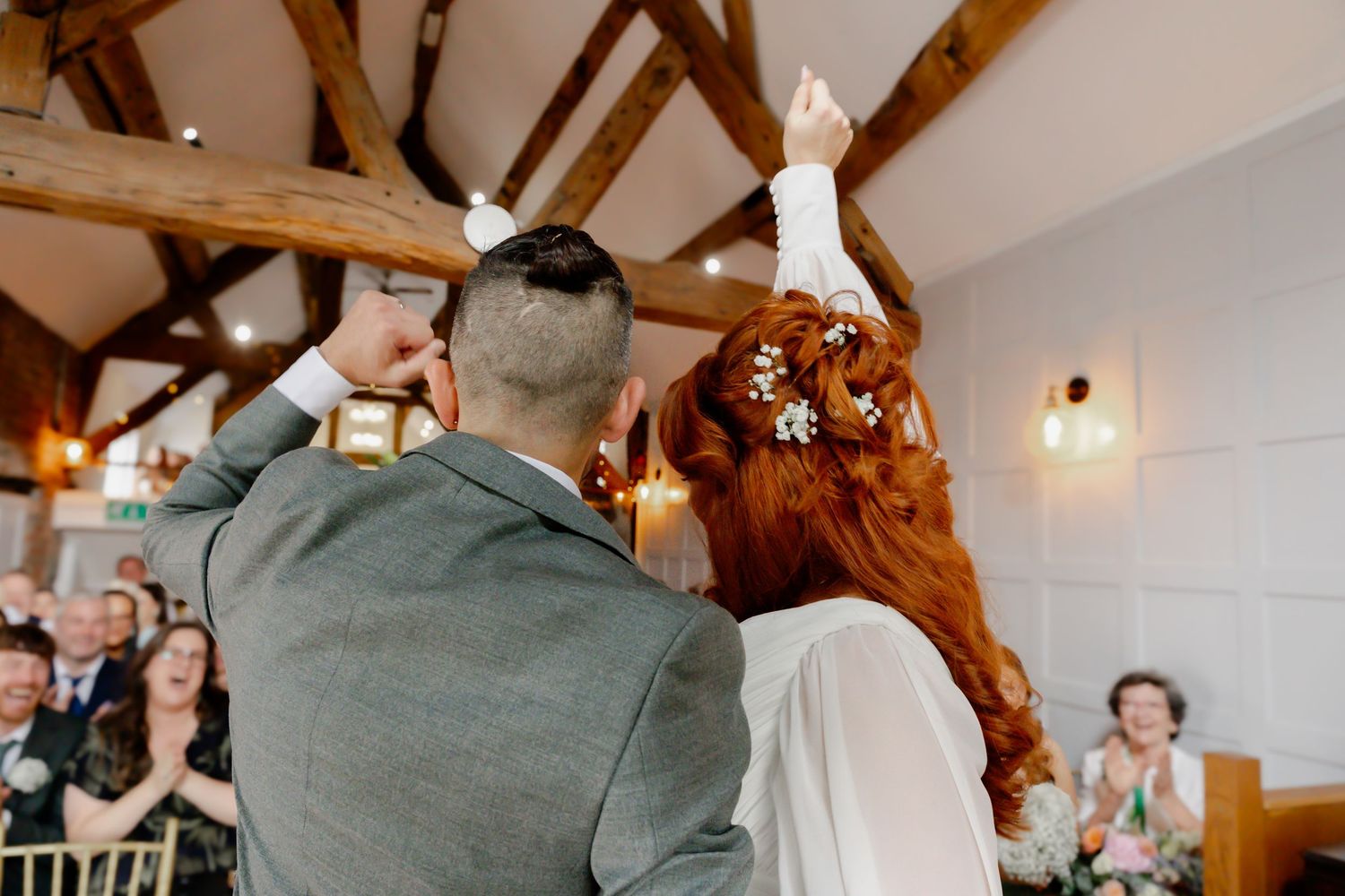 Bride with red hair and groom raising hands in celebration at rustic barn wedding ceremony.