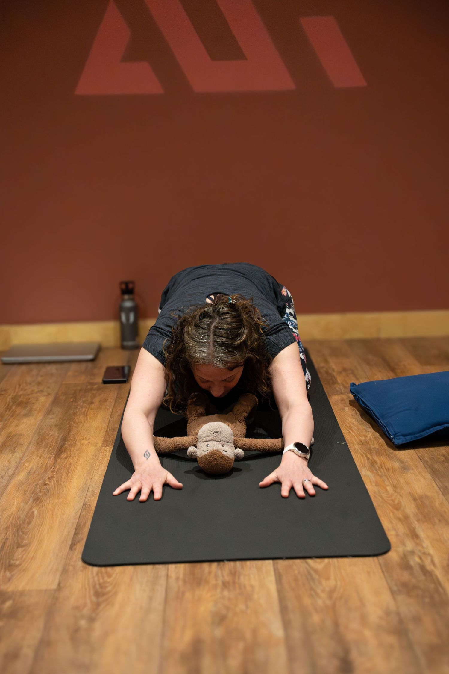 Person practicing child's pose yoga stretch on a black mat in a studio with wooden floors.