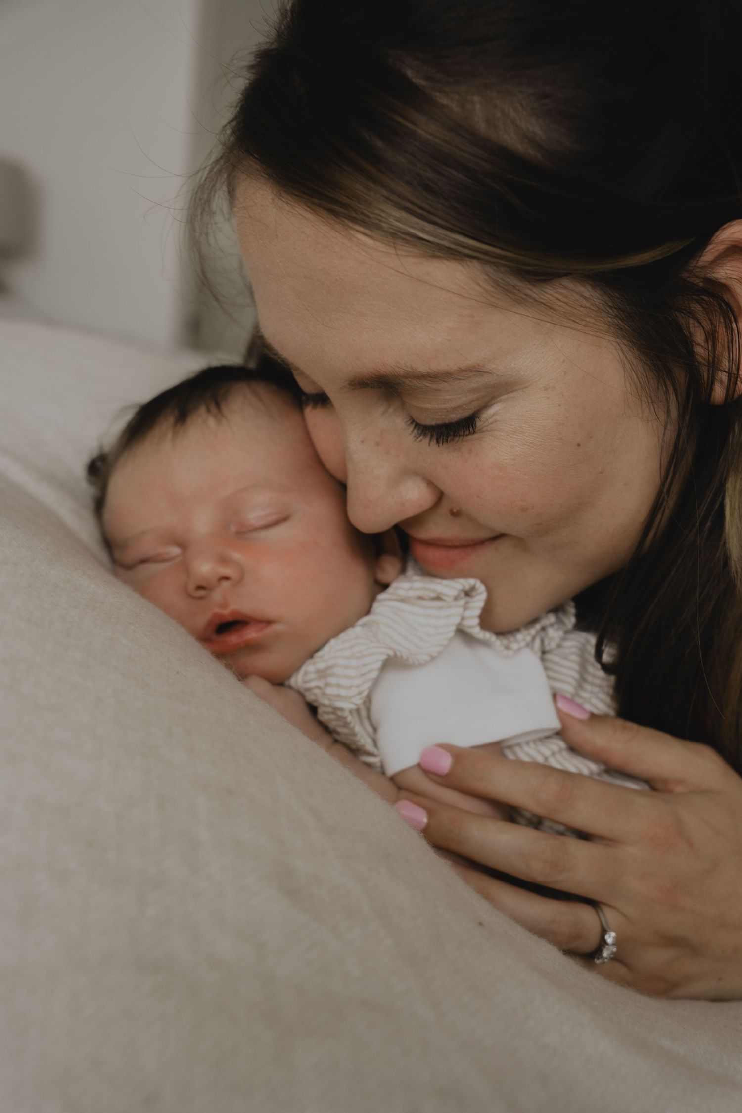 A smiling mother gently nuzzles her sleeping newborn baby while cradling them close.