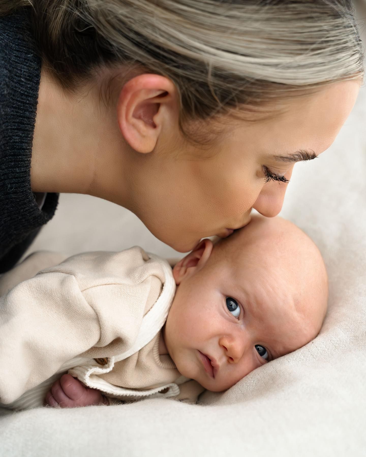 Loving mother gently kissing her newborn baby on the forehead on a white blanket.