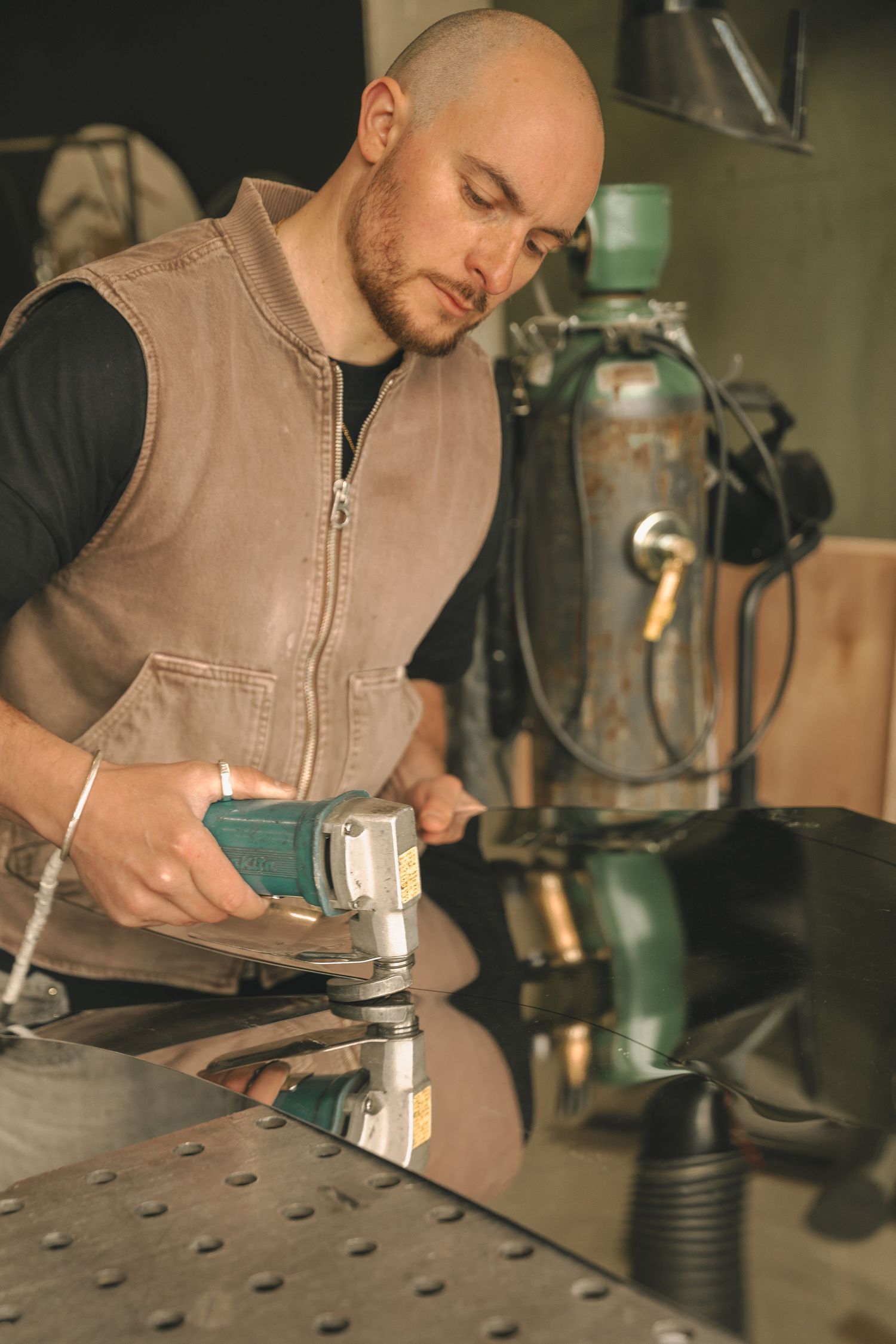 Skilled bald artisan operating angle grinder on shiny metal workbench in professional workshop.