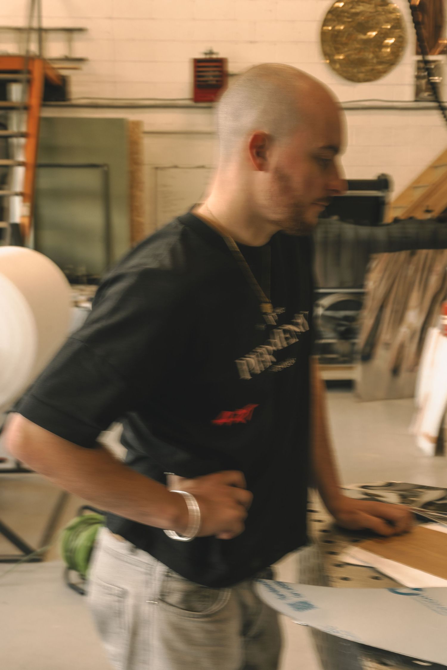 A bald man in a black graphic t-shirt moves through an art studio surrounded by large circular artworks.