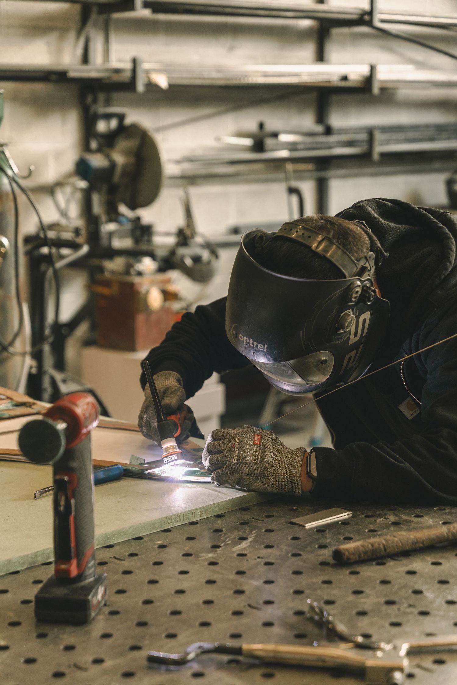 A welder wearing a protective helmet and gloves performs precision welding on a metal surface in a workshop.