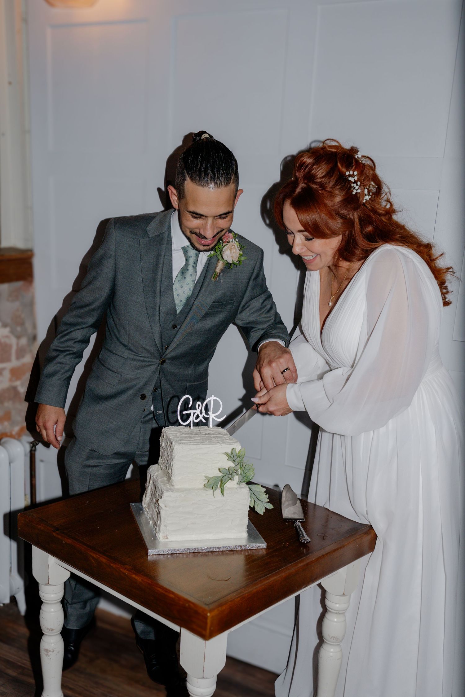 Bride and groom cutting white two-tier wedding cake together at their reception.
