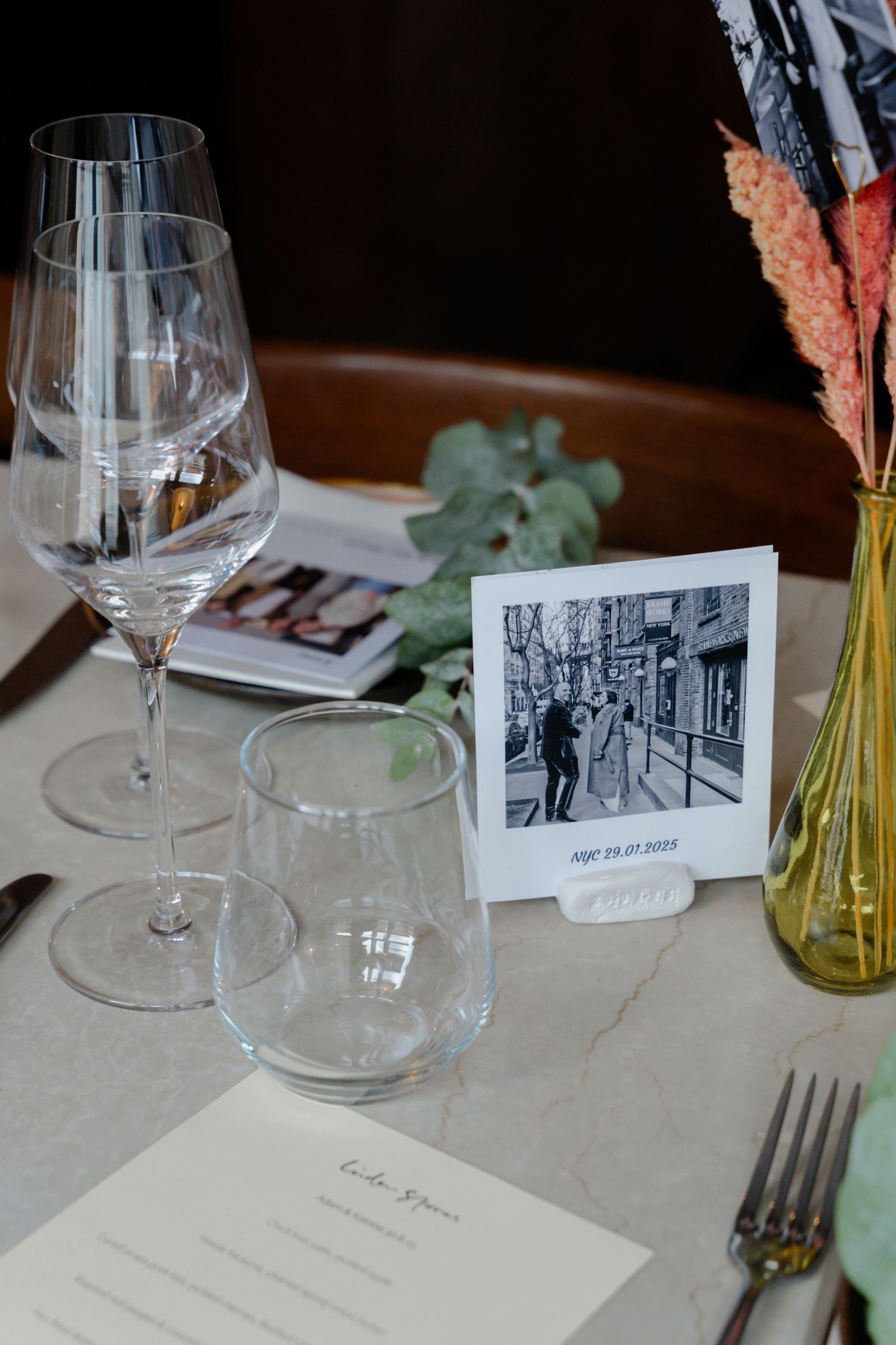 Wedding table setting with wine glasses, polaroid photo keepsake, and dried floral arrangement.