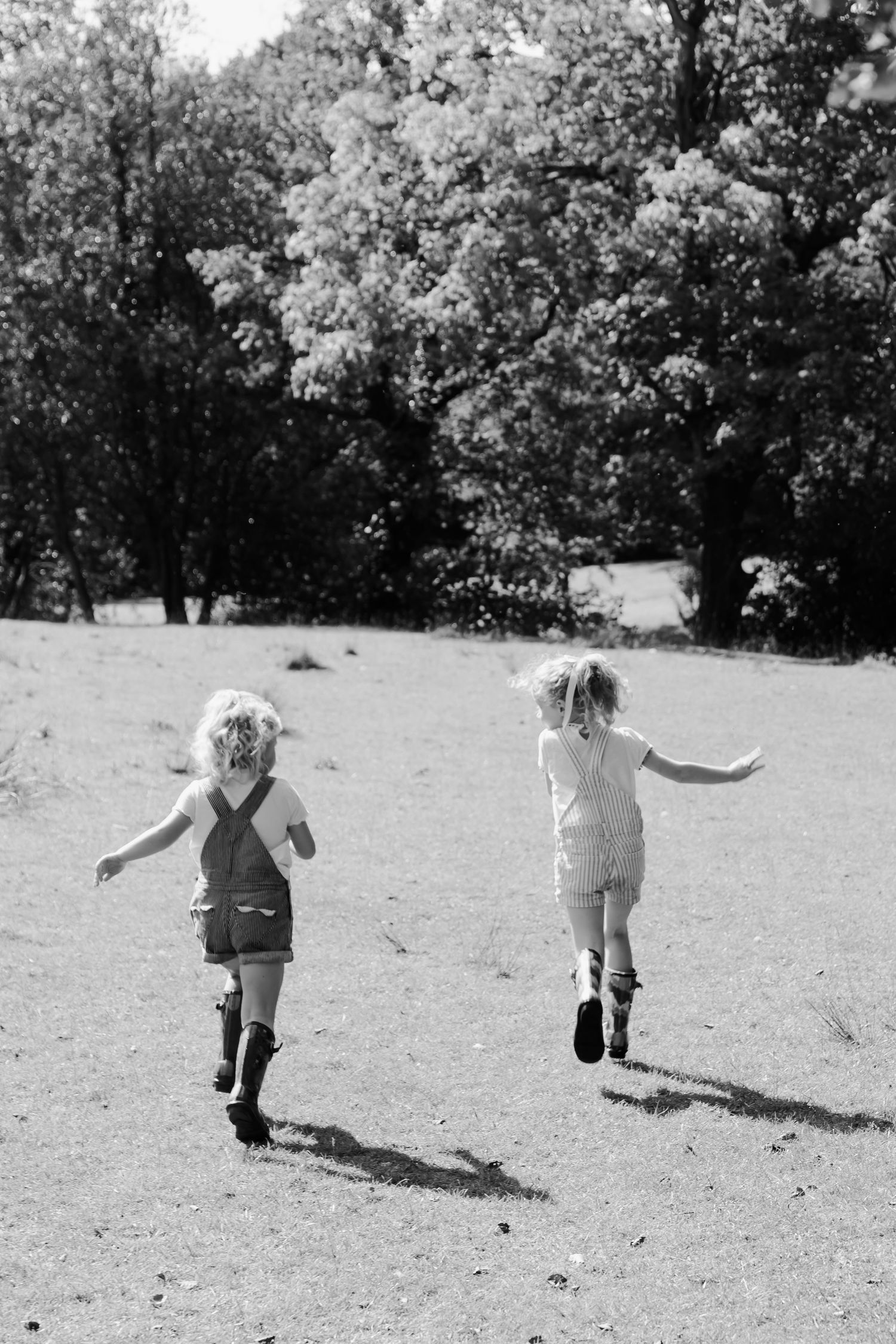 Two young blonde children running freely through a sunny field with trees in black and white photo.
