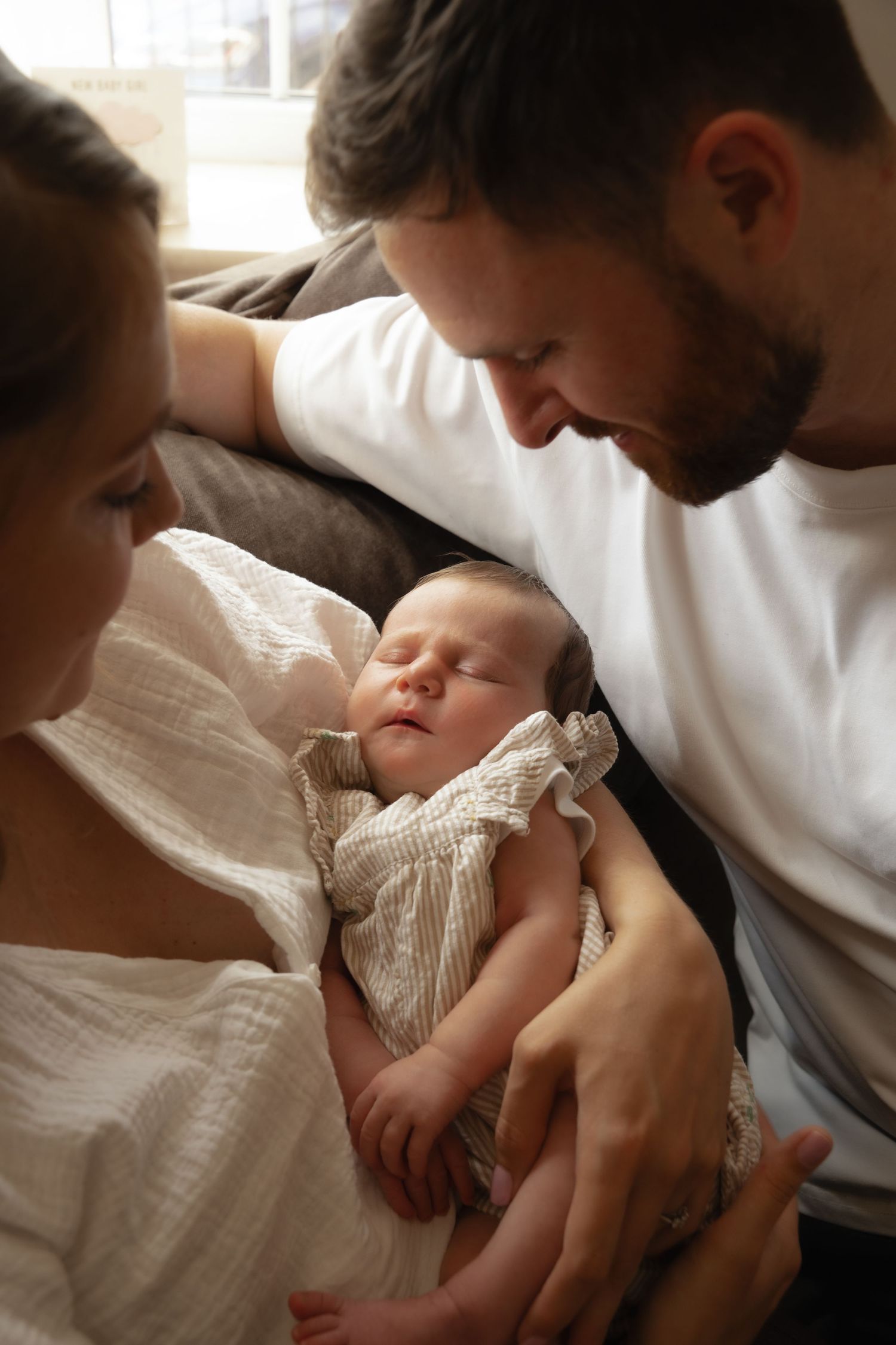 New parents lovingly gaze at their sleeping newborn baby wrapped in a white muslin cloth.