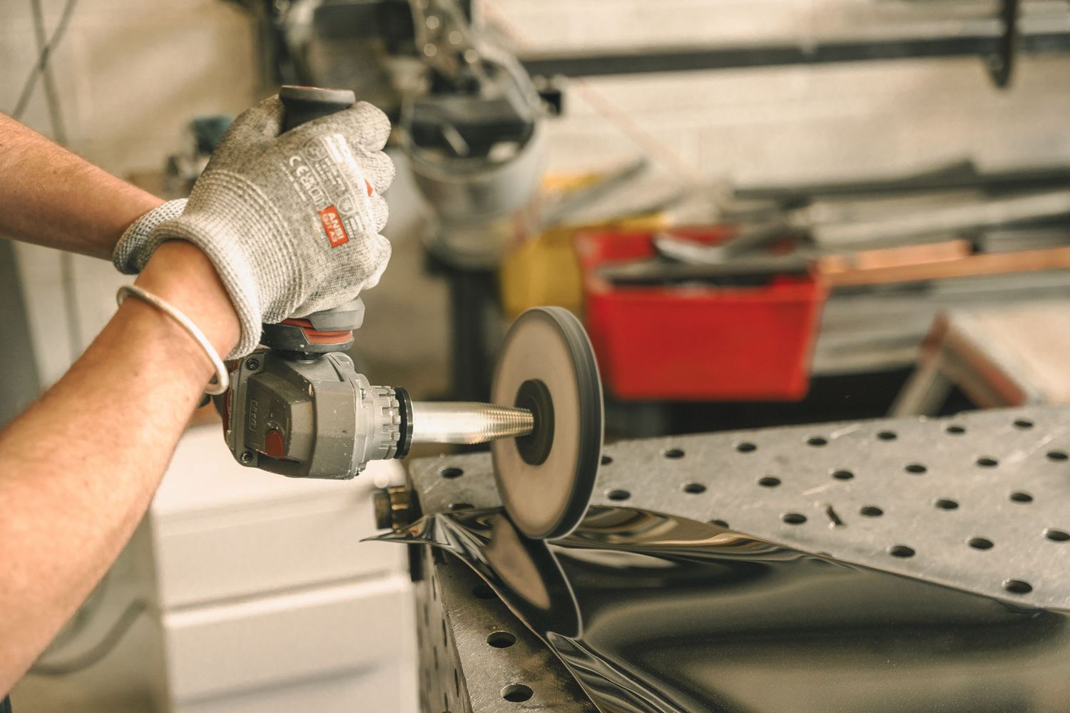 Close-up of gloved hands using an angle grinder on a dark metal piece at a workshop table.
