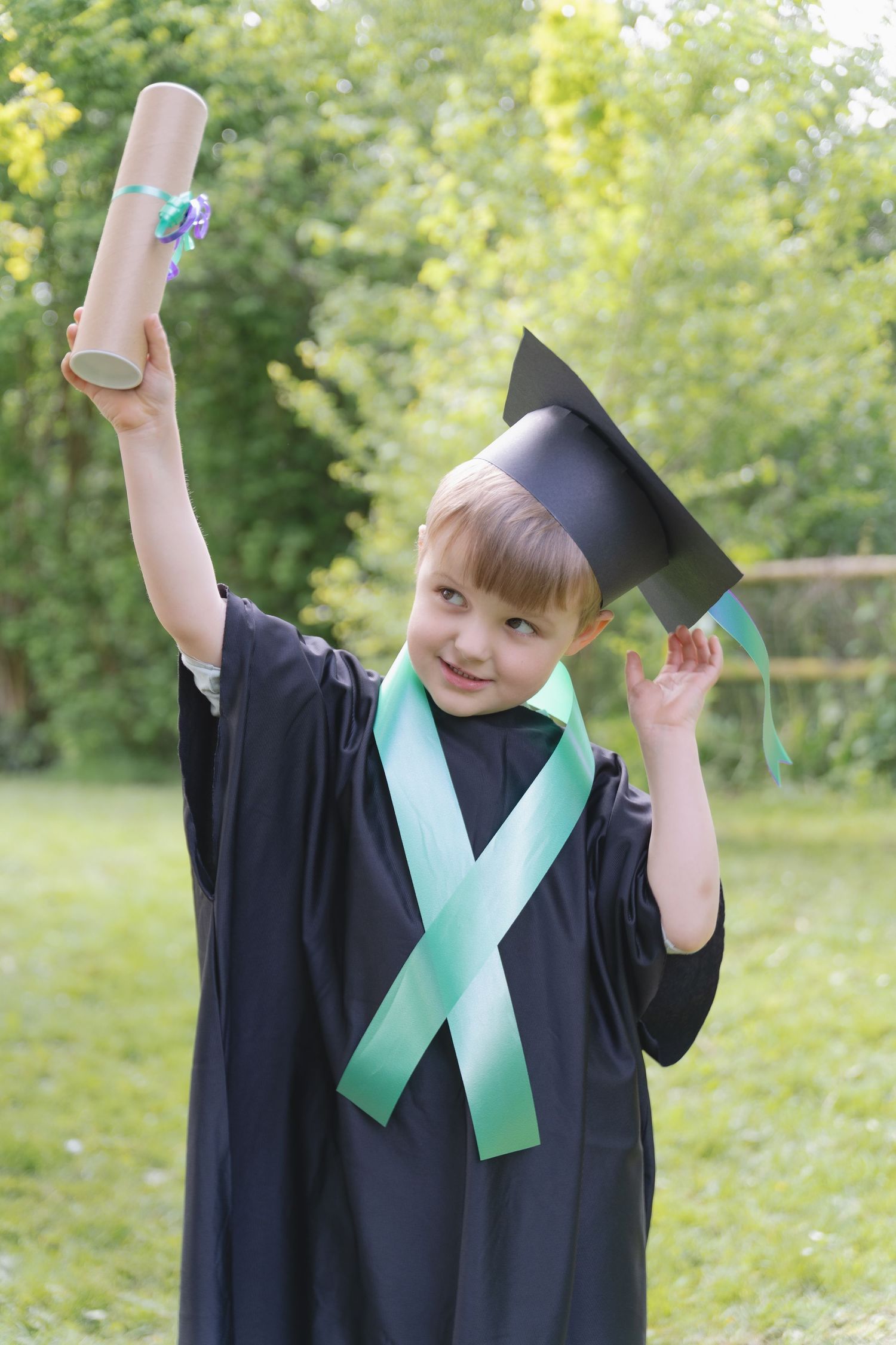Happy child in graduation gown and cap holding diploma outdoors.