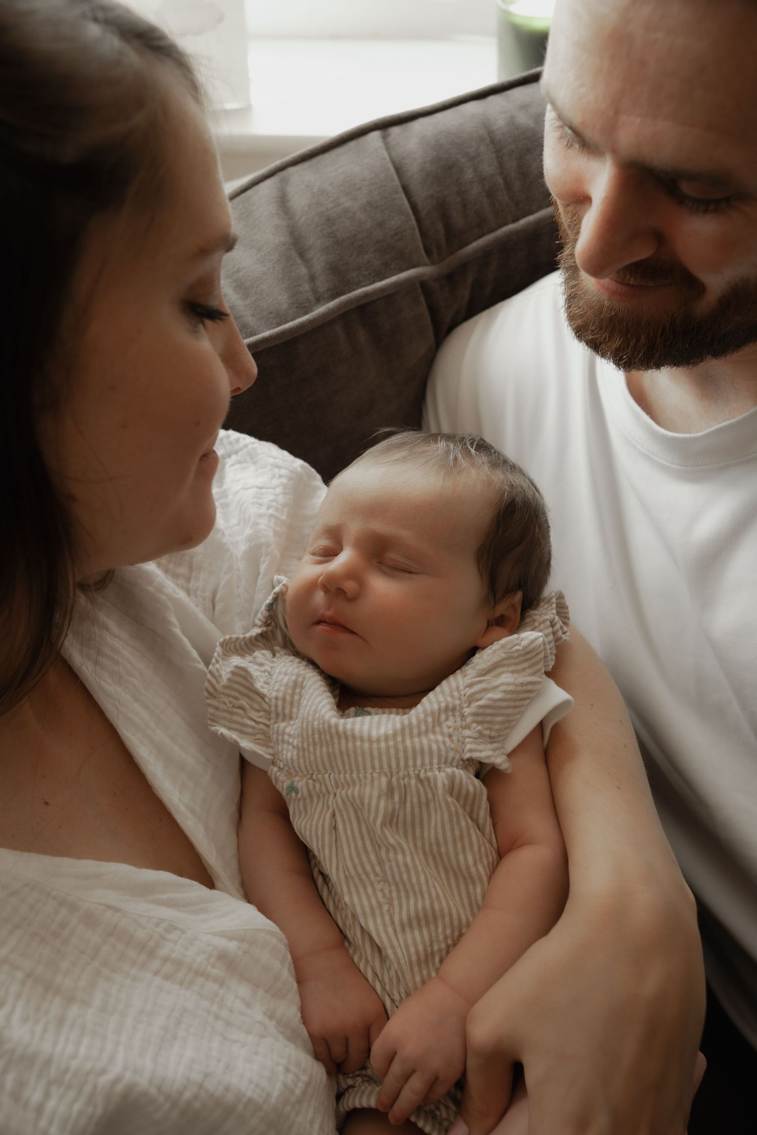 New parents lovingly gaze at their sleeping newborn baby dressed in a striped romper.