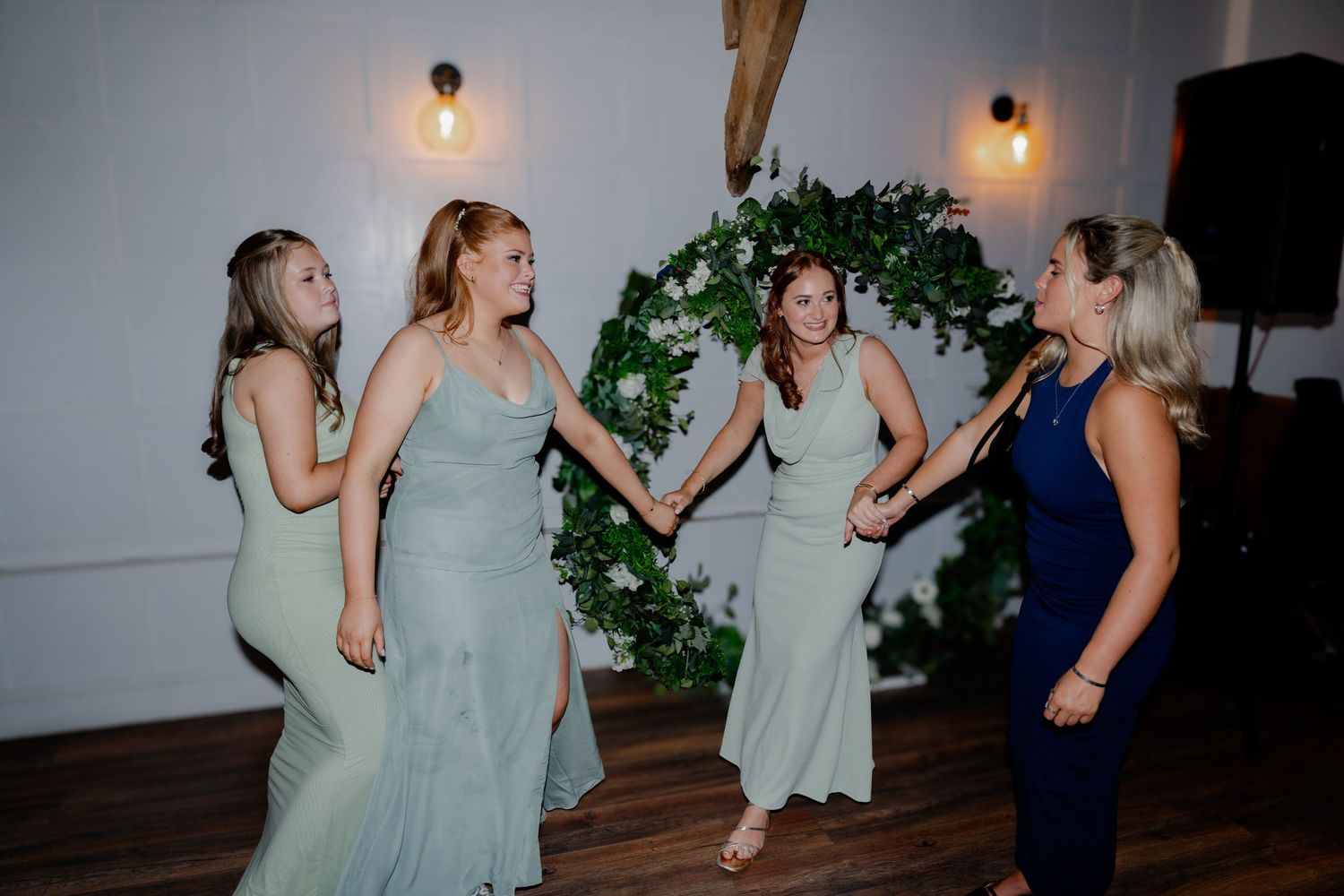 Four bridesmaids in sage green dresses dancing joyfully at a wedding reception.