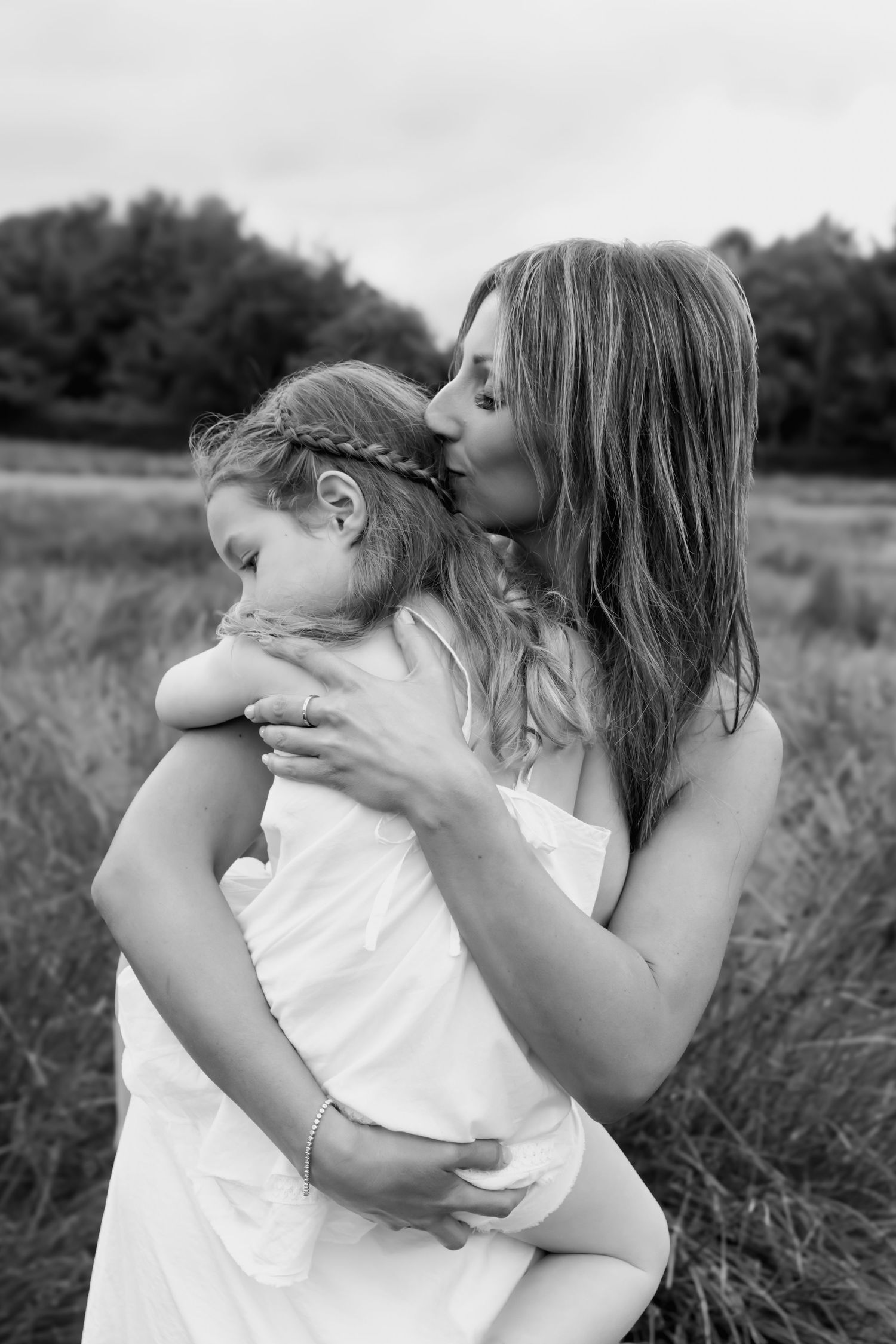 Black and white photo of a mother kissing her daughter in a field.