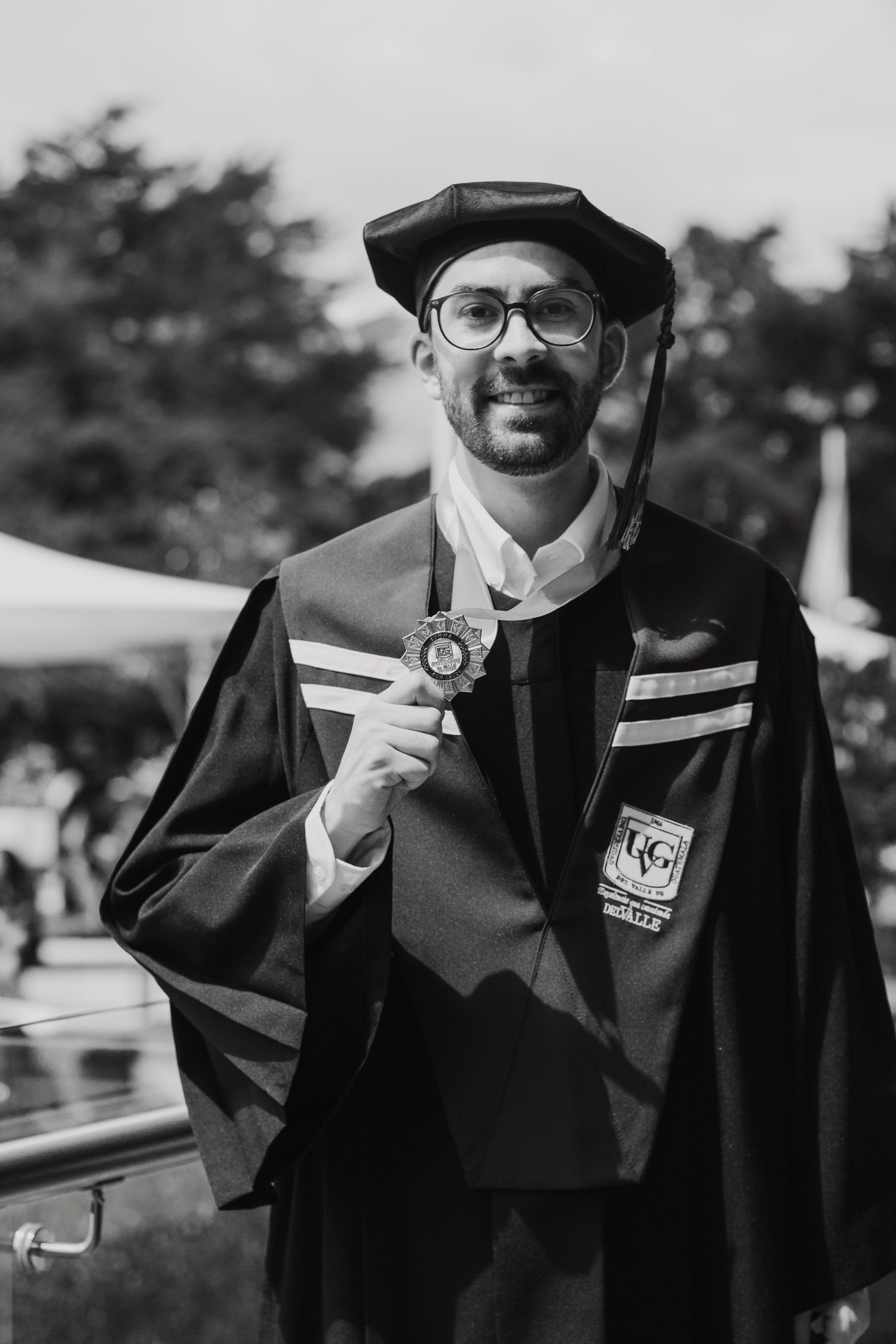 A graduate in traditional black academic regalia and cap holds up their diploma while smiling during commencement.