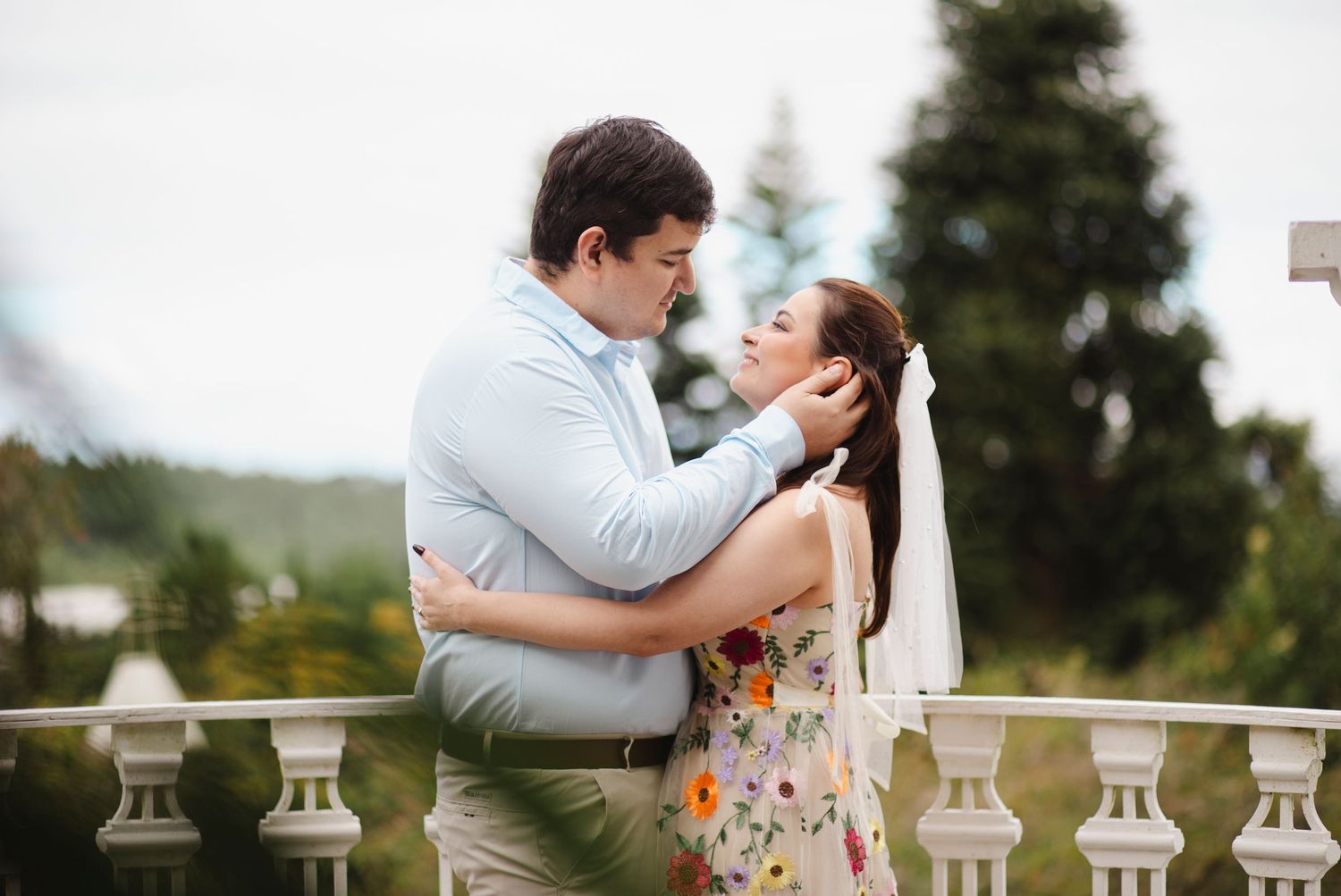 A romantic couple shares an intimate moment on a stone balcony overlooking a scenic landscape.