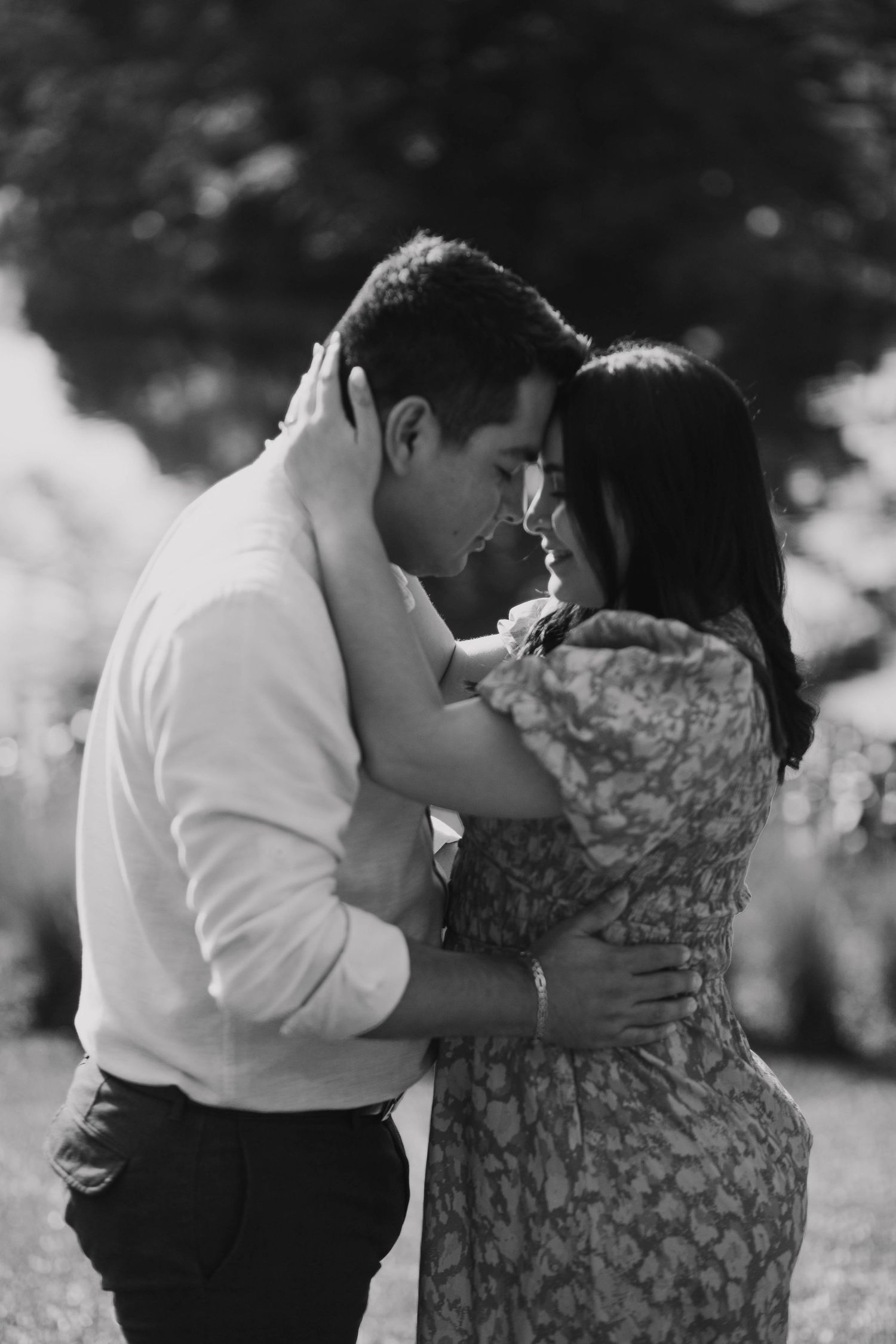 An intimate black and white portrait of a couple in a tender embrace outdoors.