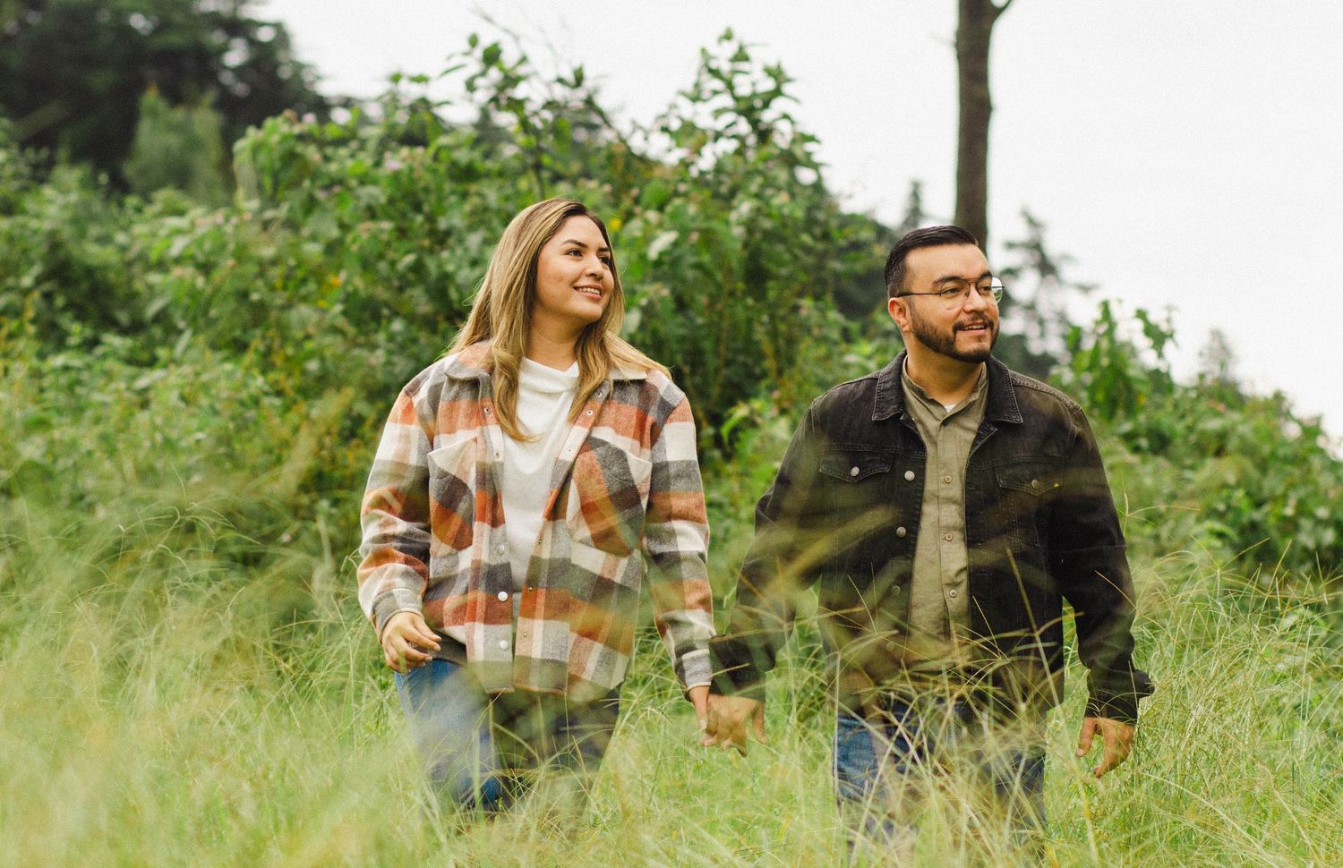 Candid shot of couple walking through tall grass in casual outdoor wear.