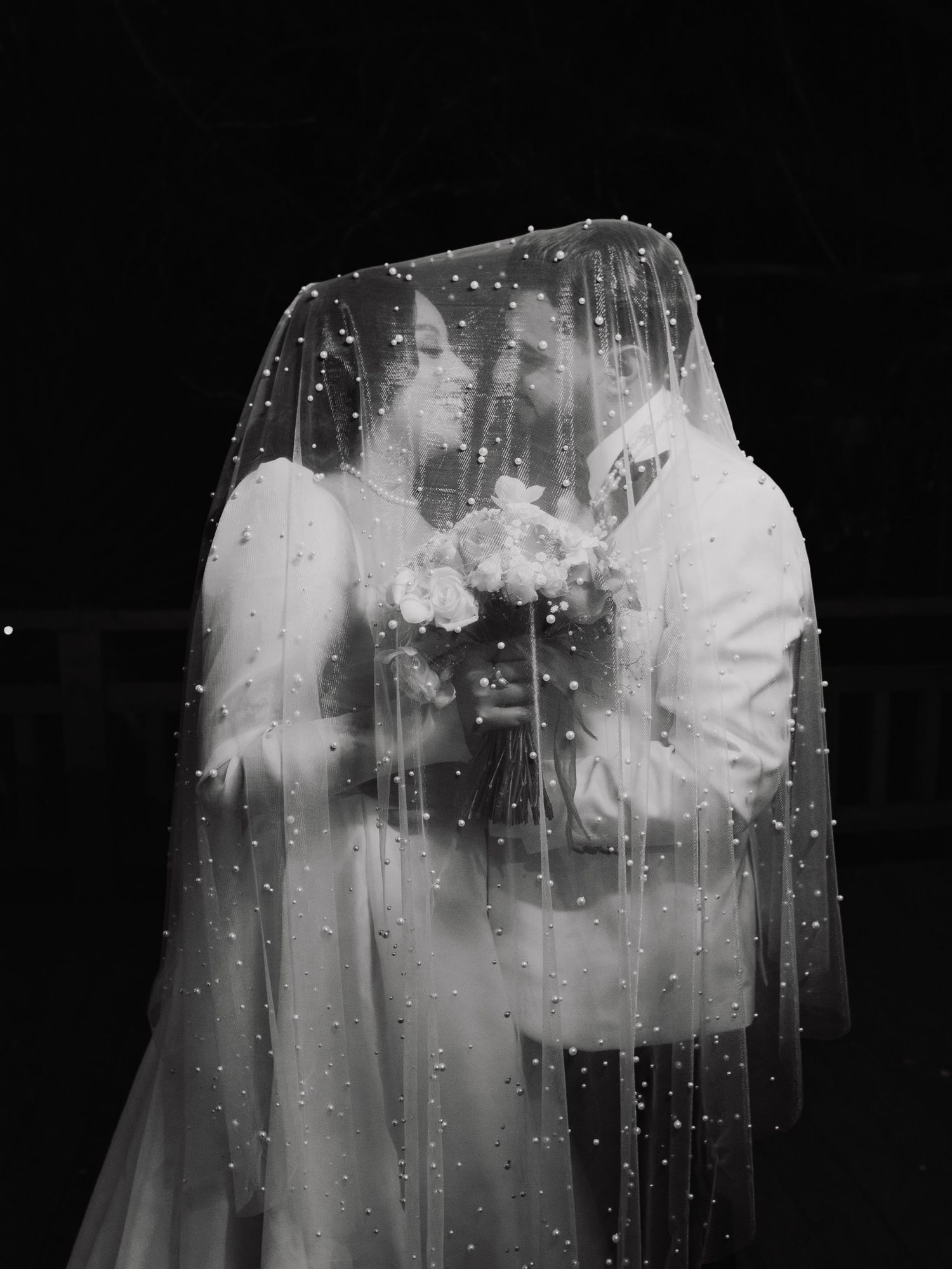 Artistic black and white wedding photo with rain drops on veil creating dreamy effect.