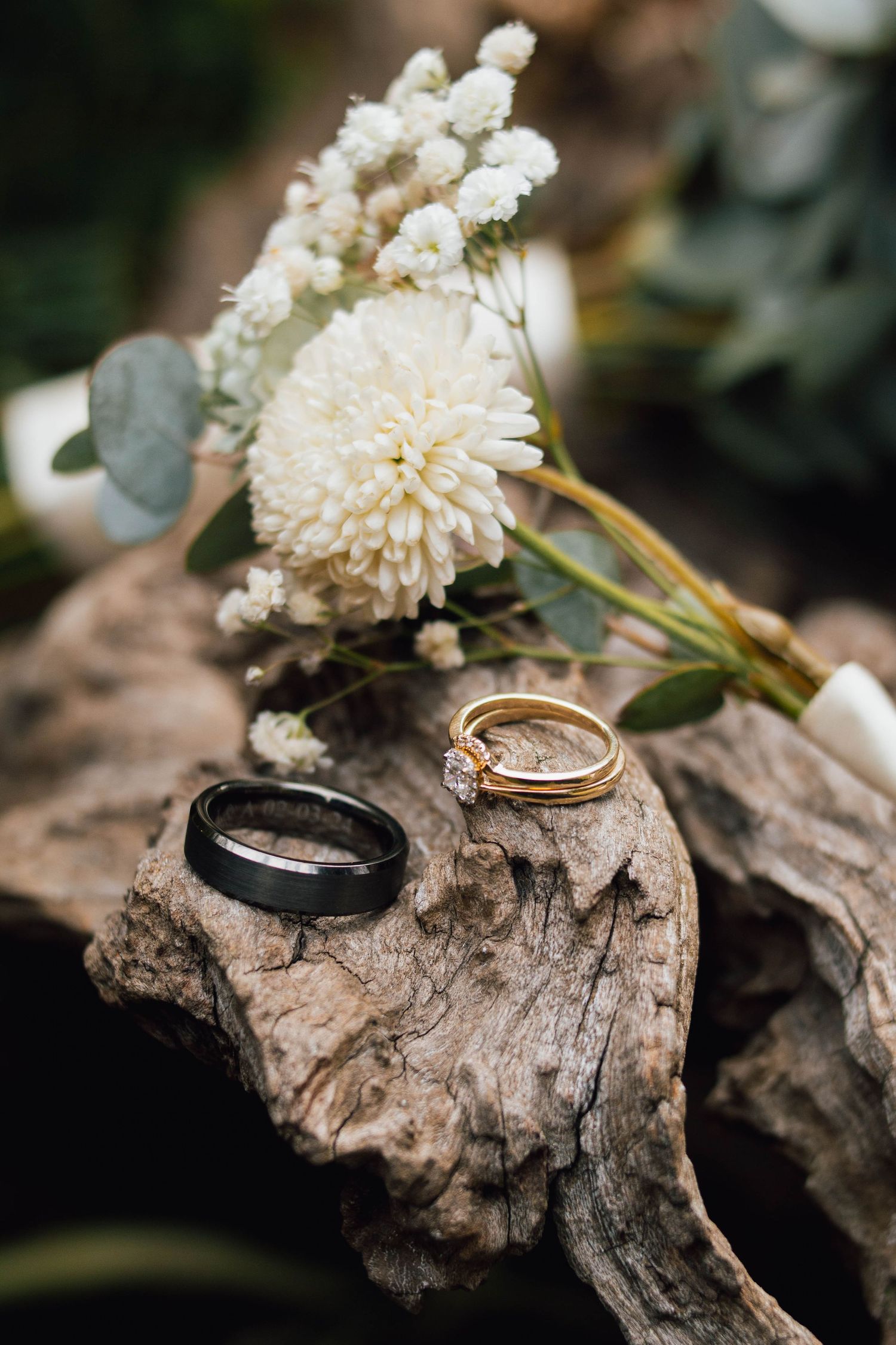 Wedding rings and white flowers arranged on weathered driftwood.