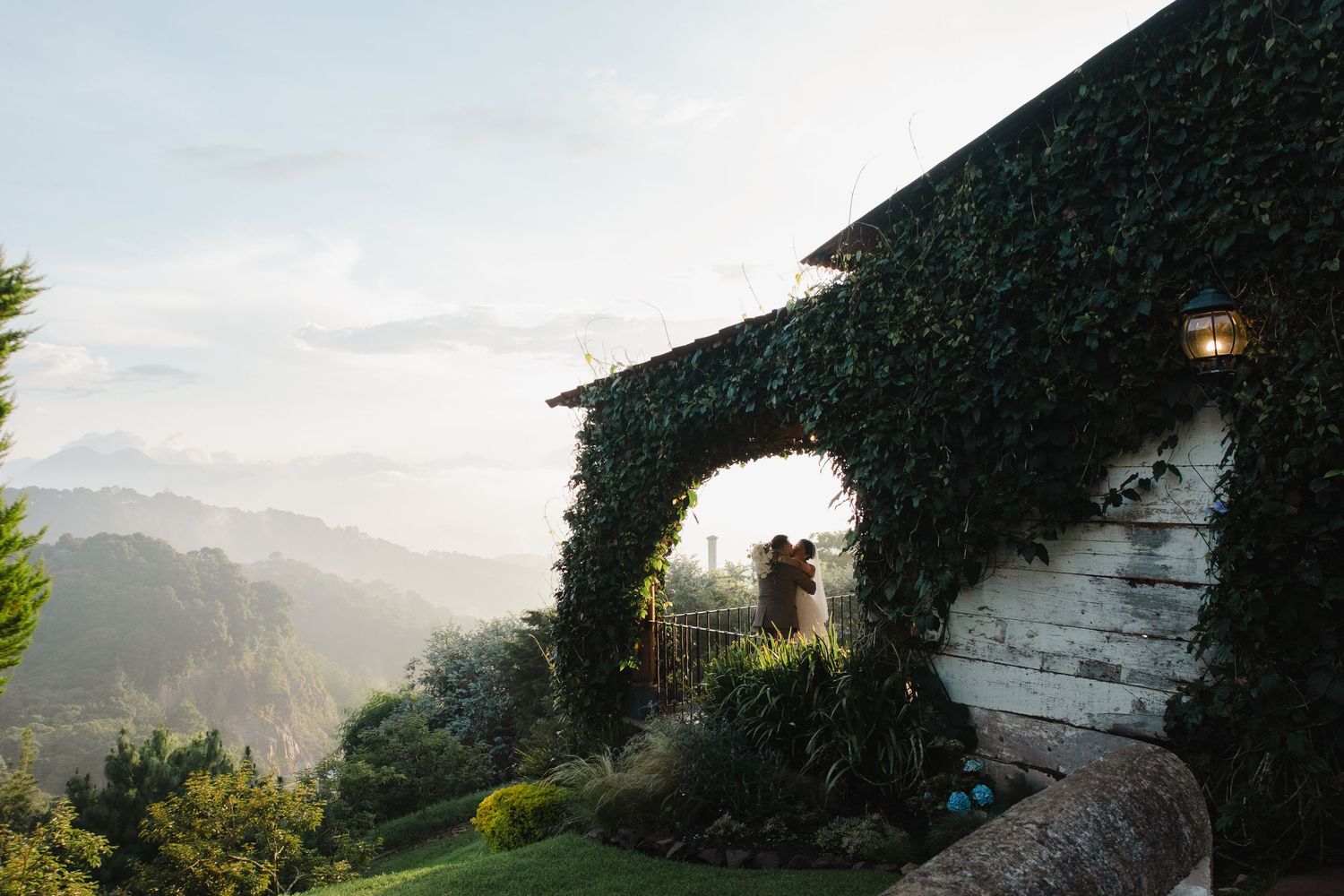A scenic mountain view through an ivy-covered stone archway with sunlight filtering through the leaves.