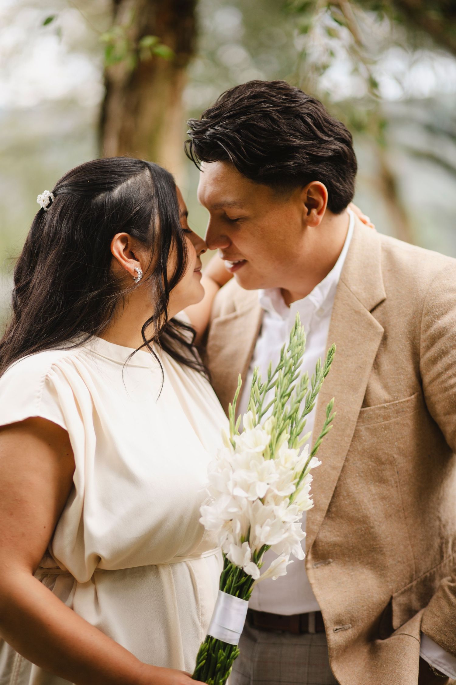 A romantic couple in neutral tones share an intimate moment outdoors against a soft, natural background.