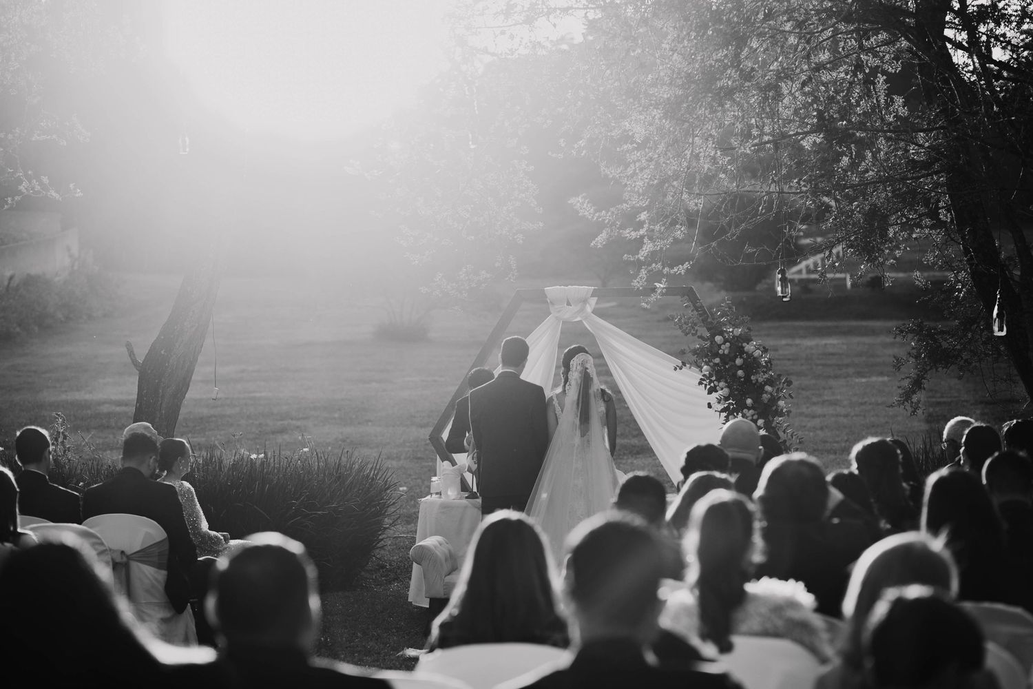 Black and white wedding ceremony photo with guests watching couple walk down aisle.