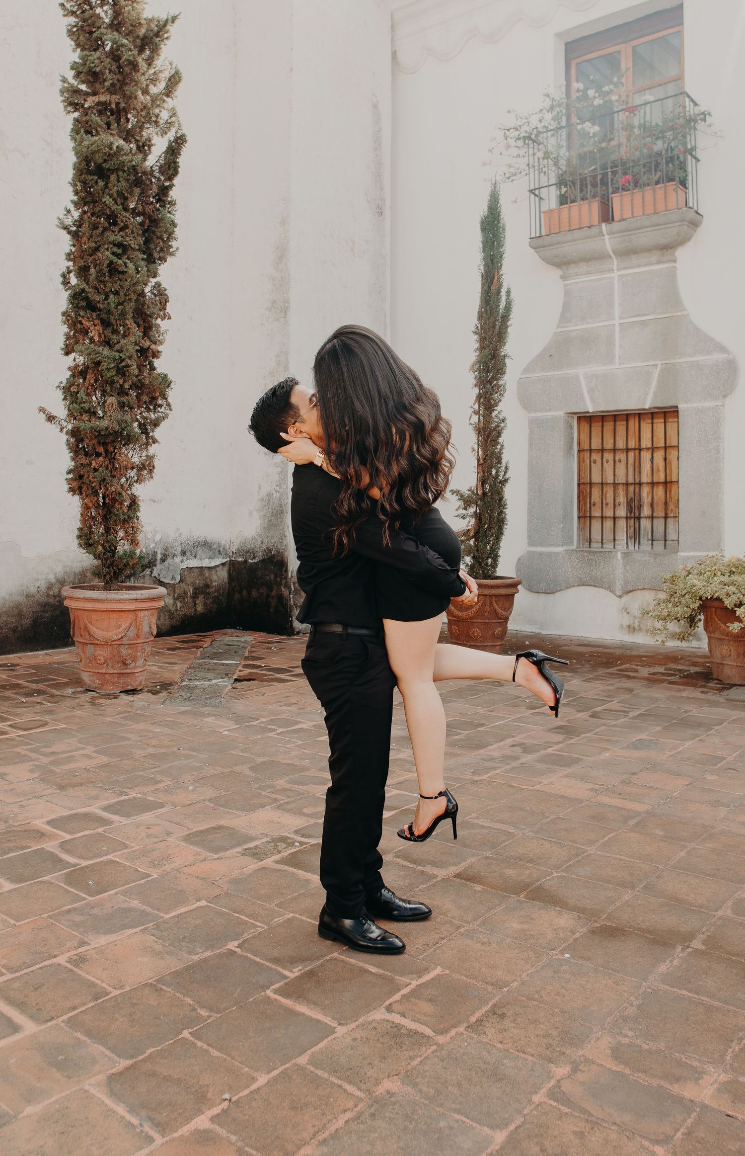 A sequence of four photos showing a person in black attire taking photos against a rustic stone wall and courtyard.