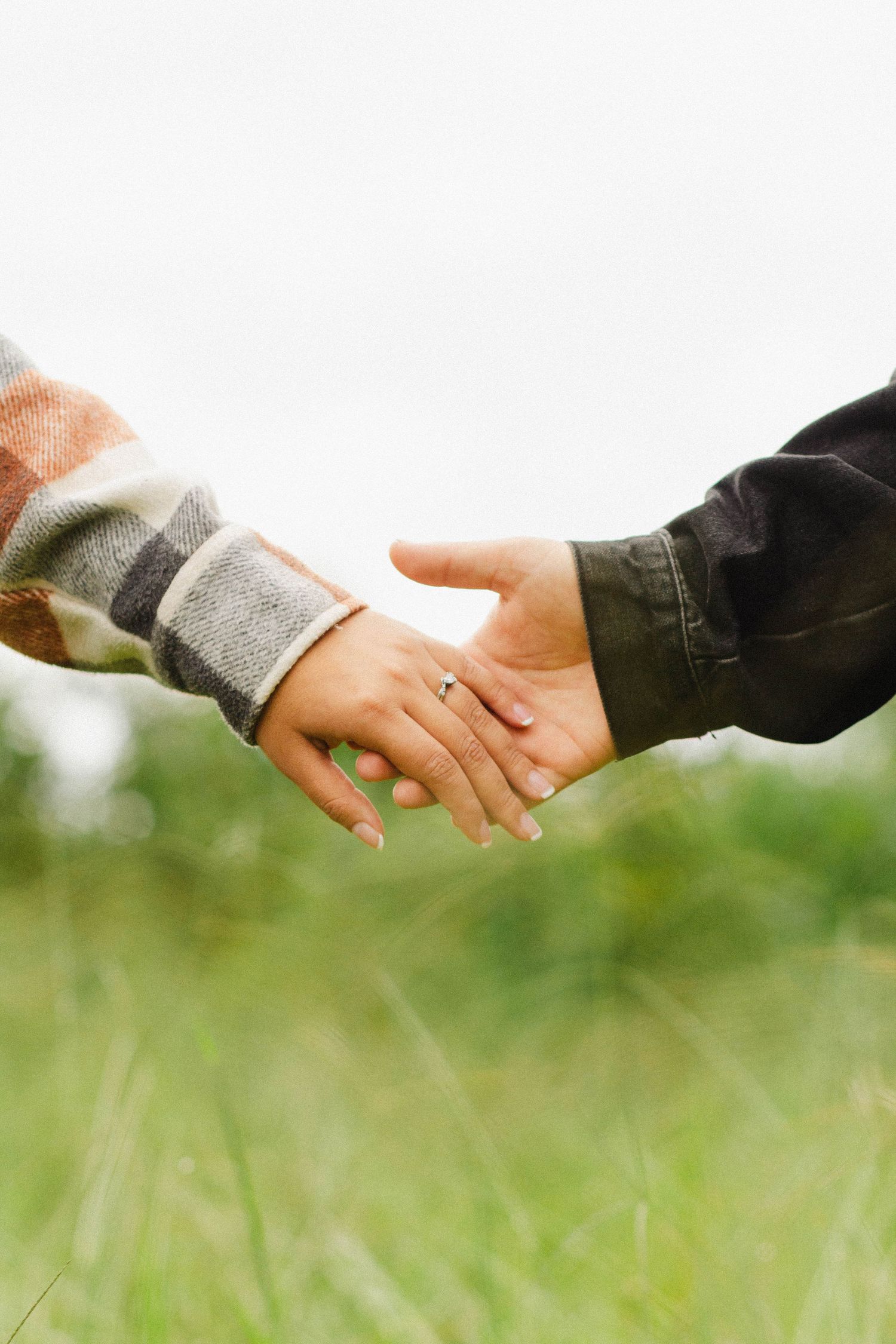 Close-up of couple holding hands in a grassy field showing engagement ring.