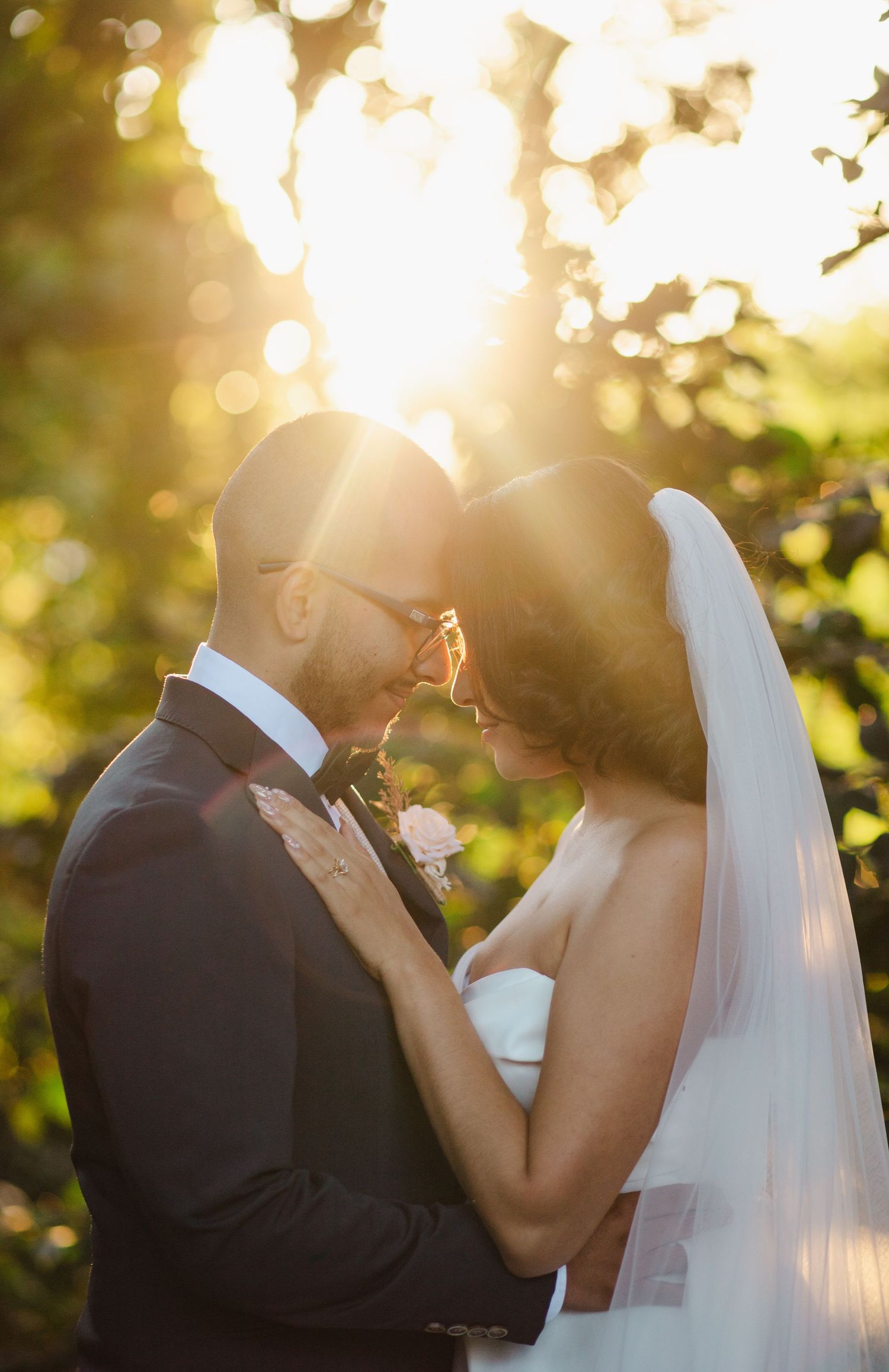 Newlywed couple shares intimate moments at sunset with beautiful golden bokeh lighting in the background.