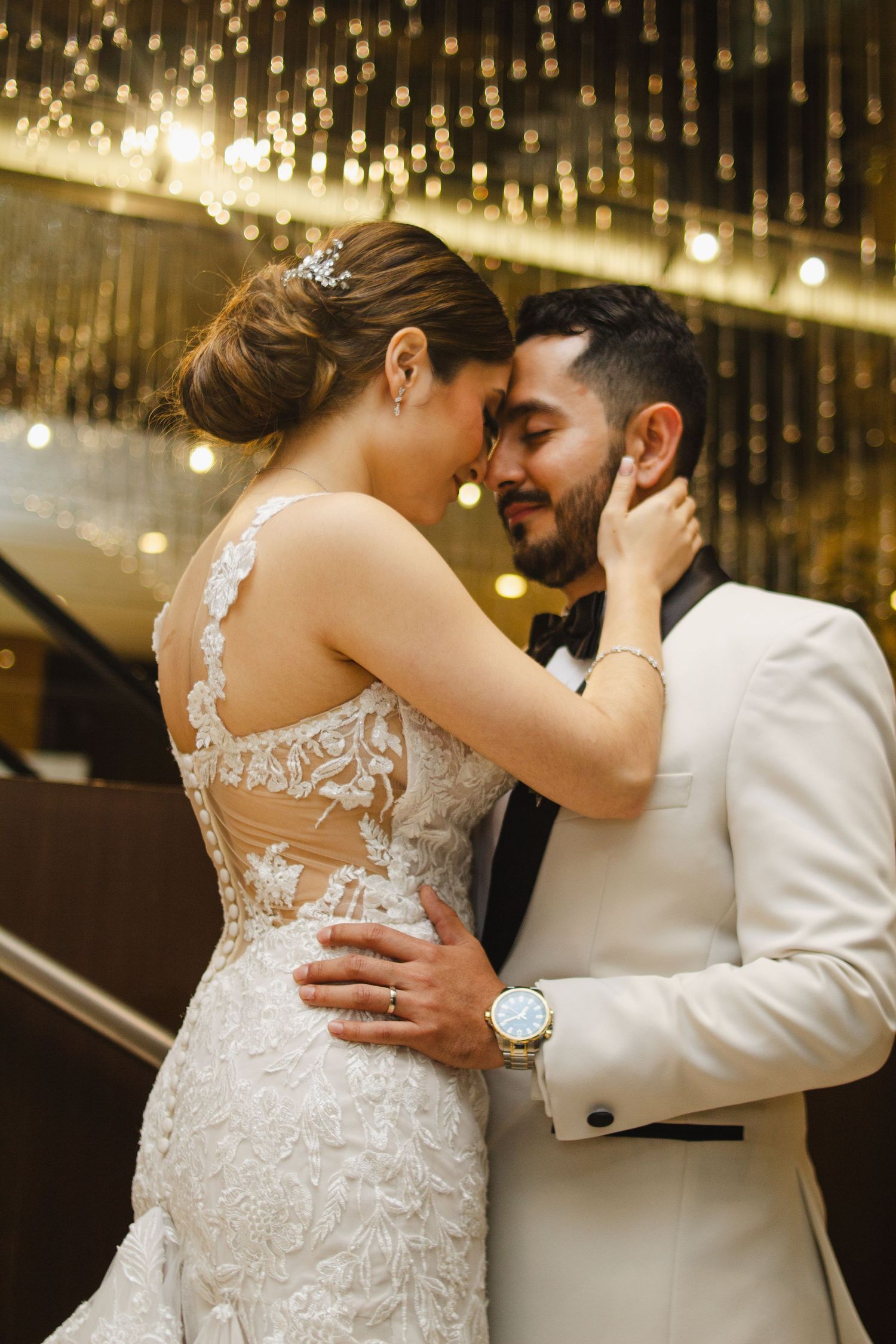Romantic wedding scene with couple embracing under golden string lights and bride wearing detailed lace gown.
