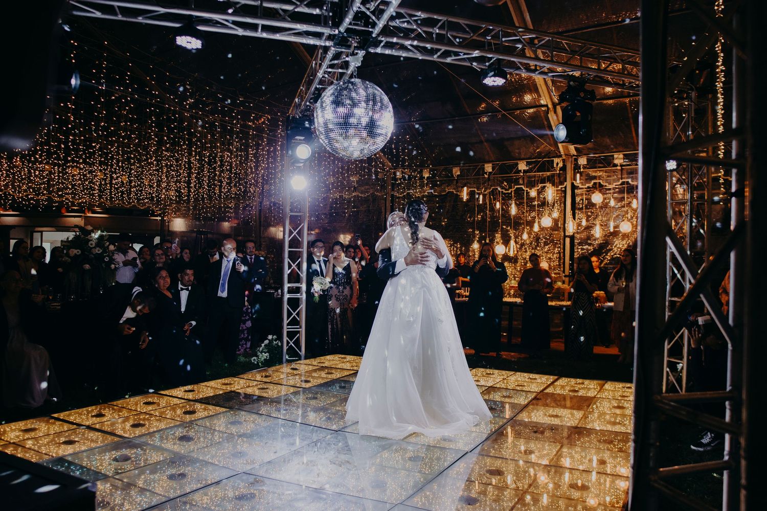 Wedding reception dance floor illuminated with disco lights and a glowing disco ball overhead.