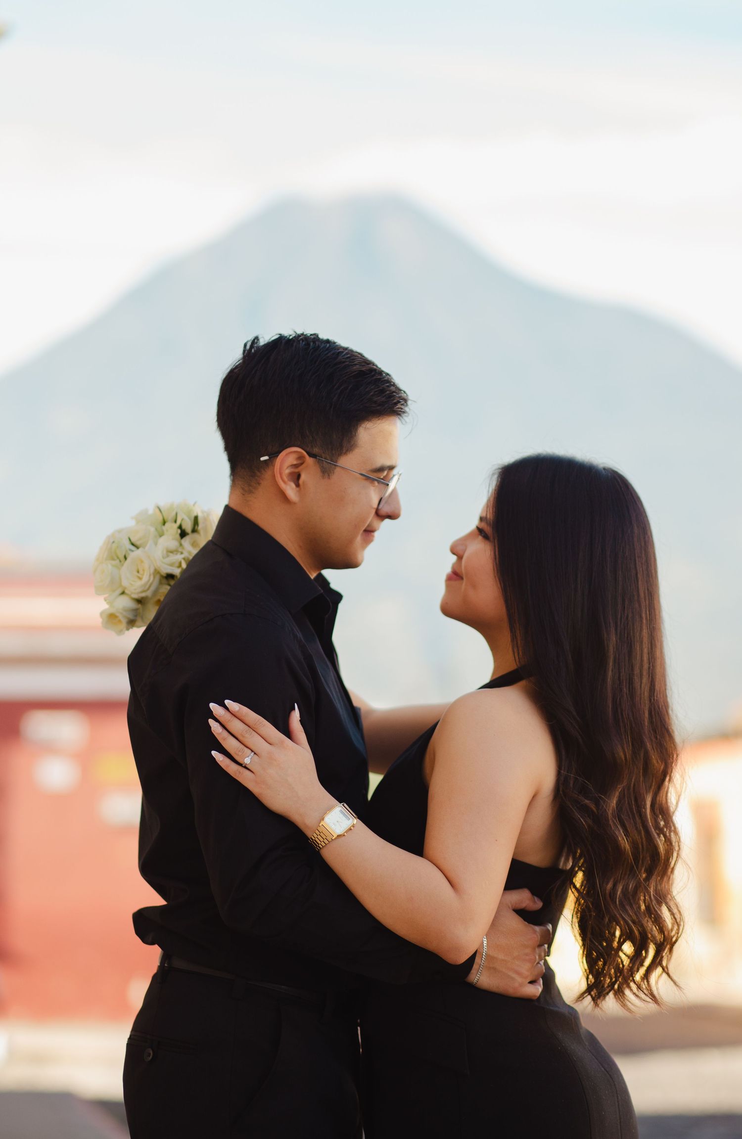 A romantic couple embraces and laughs together during a sunset photoshoot with mountains in the background.