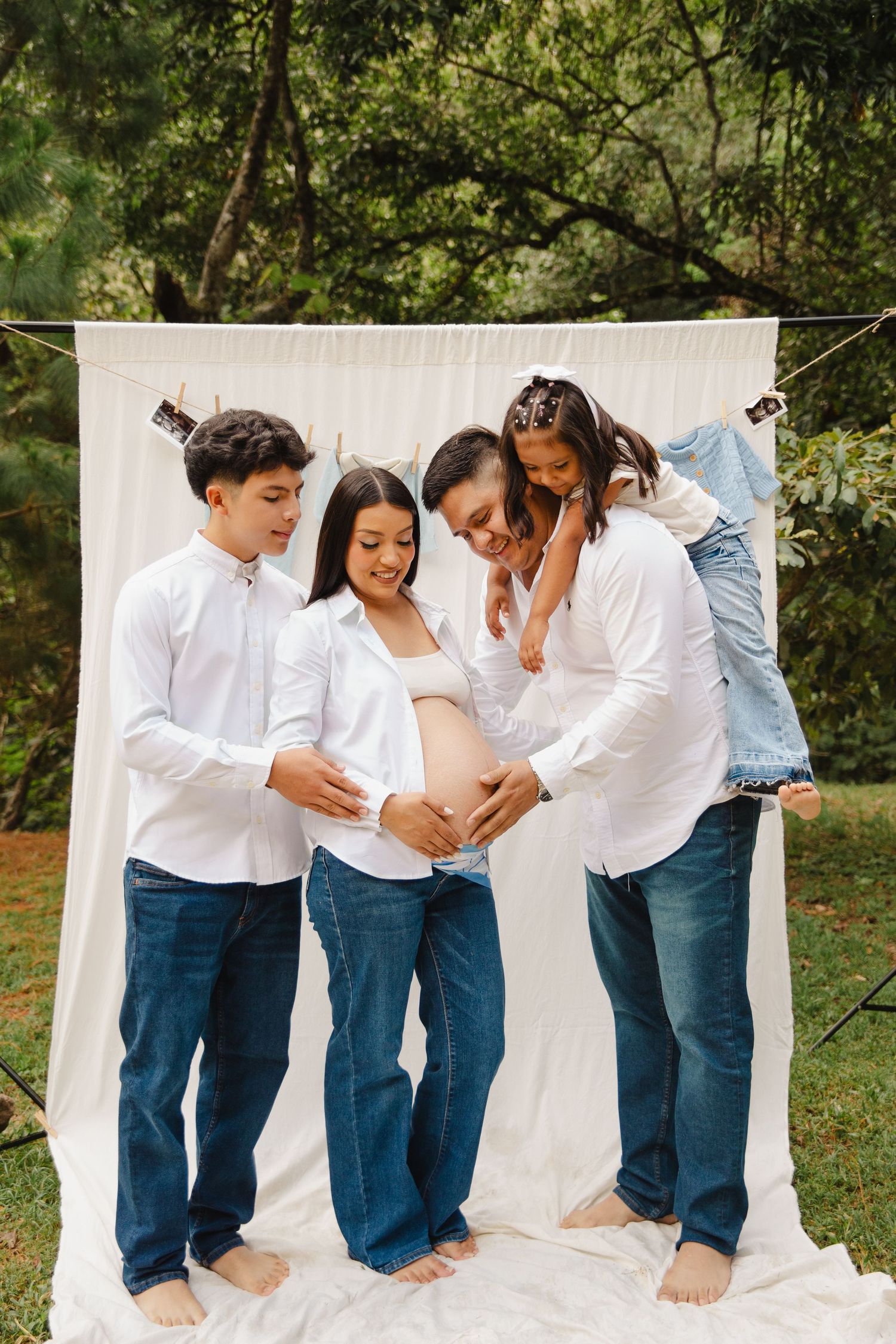 Family maternity photo shoot outdoors with pregnant mother, father, son, and daughter in white shirts and jeans.