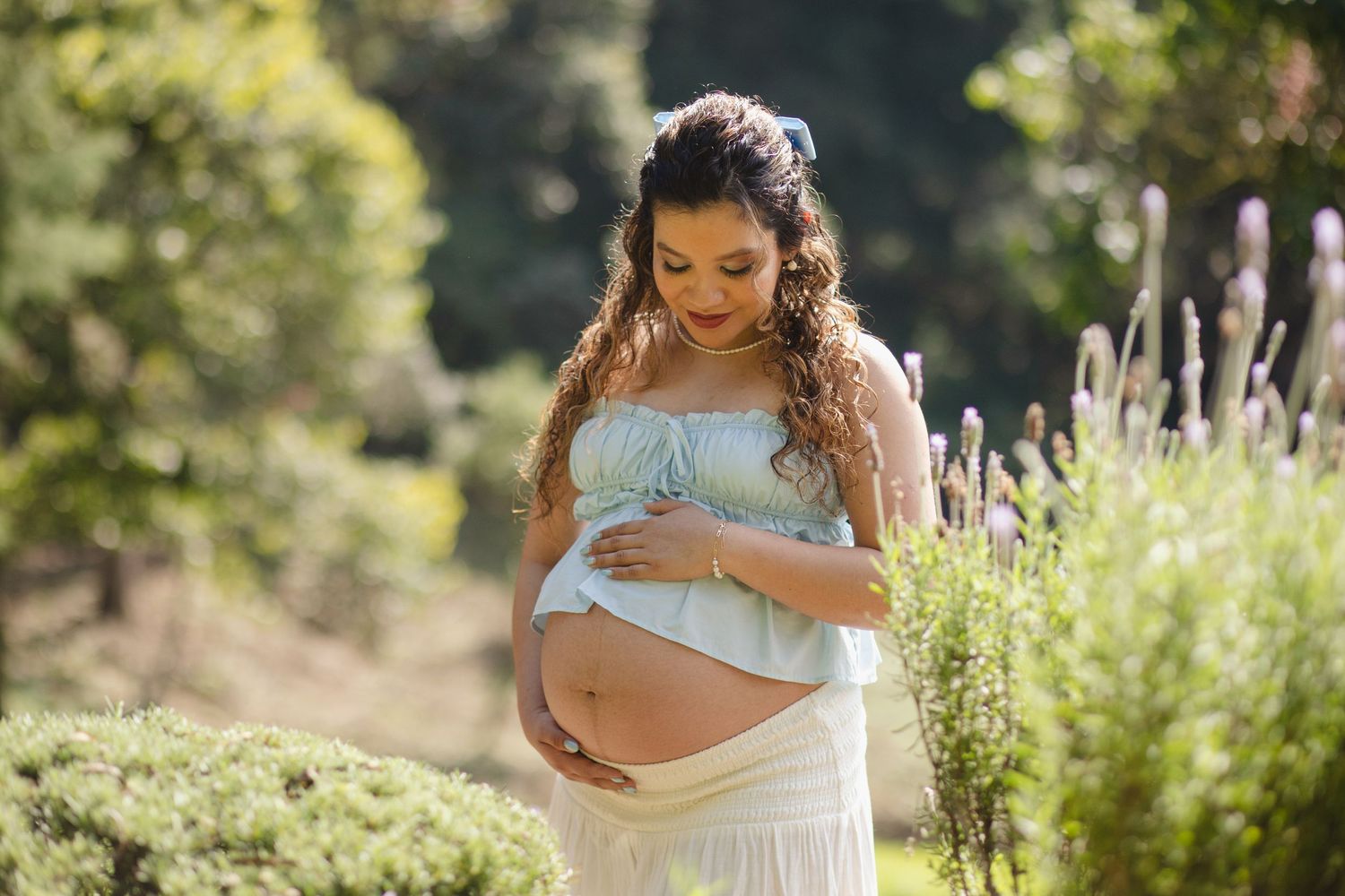 A collection of maternity photos showing someone in a white dress posing in a sunlit garden with lavender flowers.