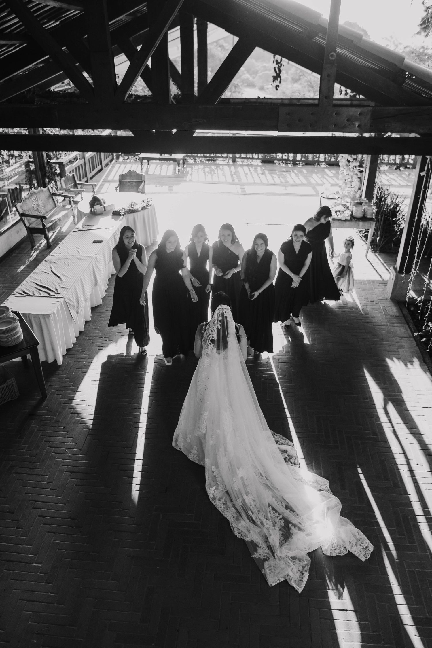 Silhouette of bridal party standing in dramatic lighting with bride's dress trailing behind.