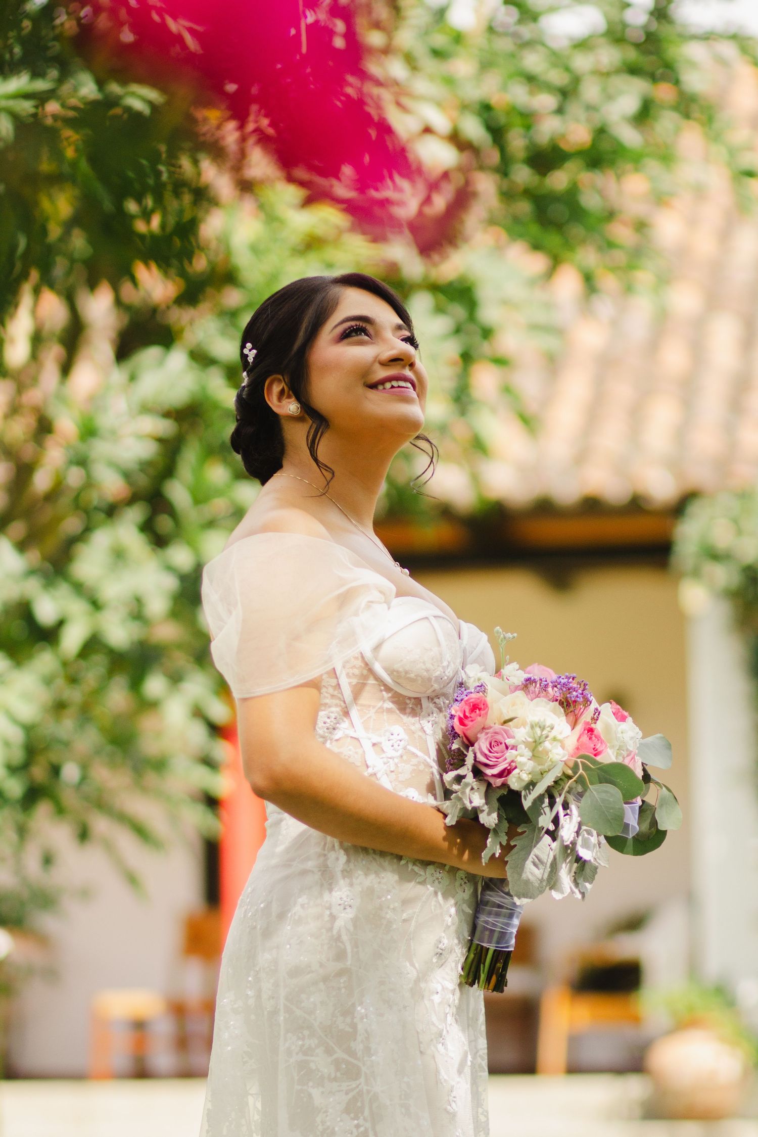 An elegant bride holding a pink and white bouquet poses in a garden setting.